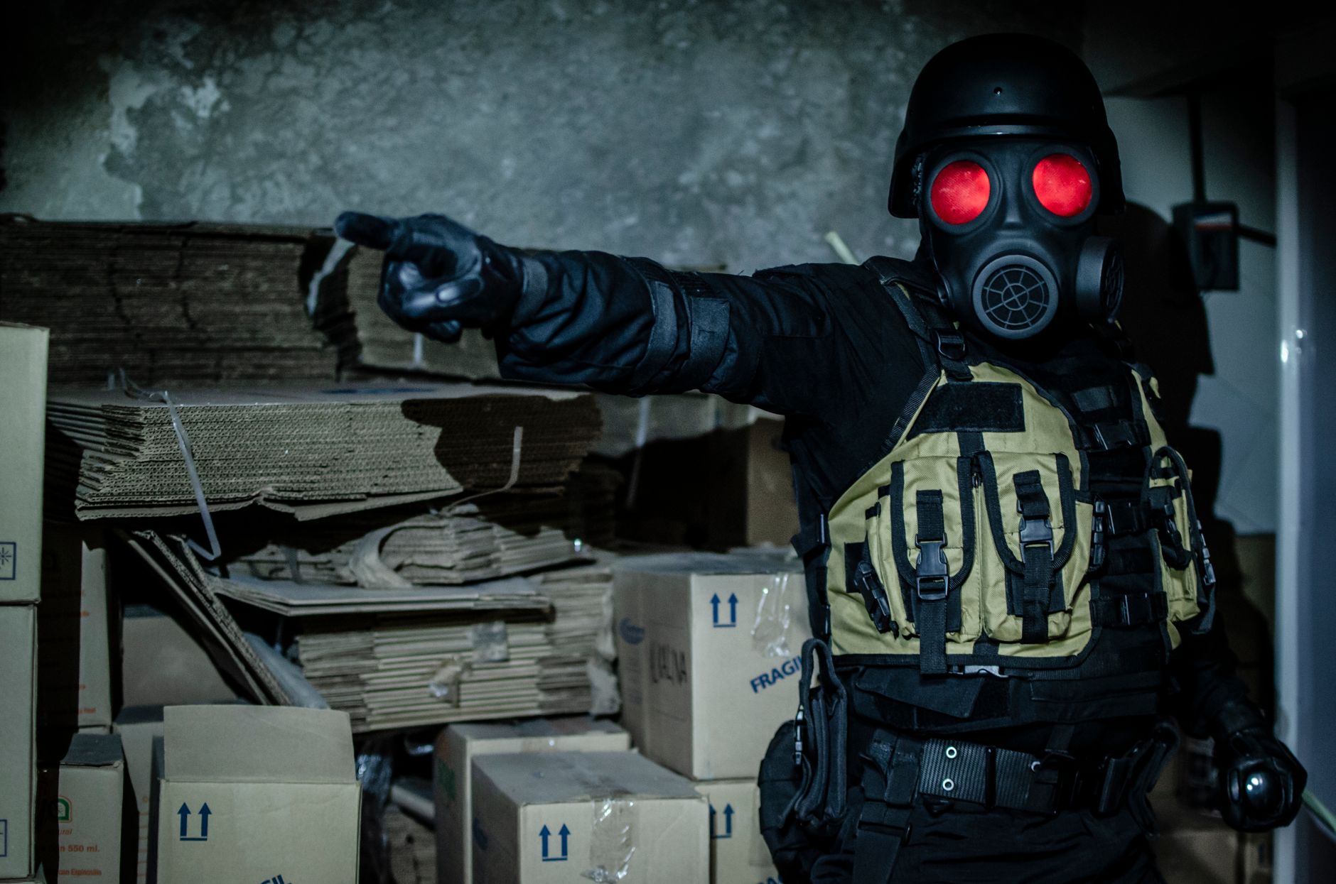 Dark and moody scene of a person in tactical gear and gas mask in an abandoned warehouse.