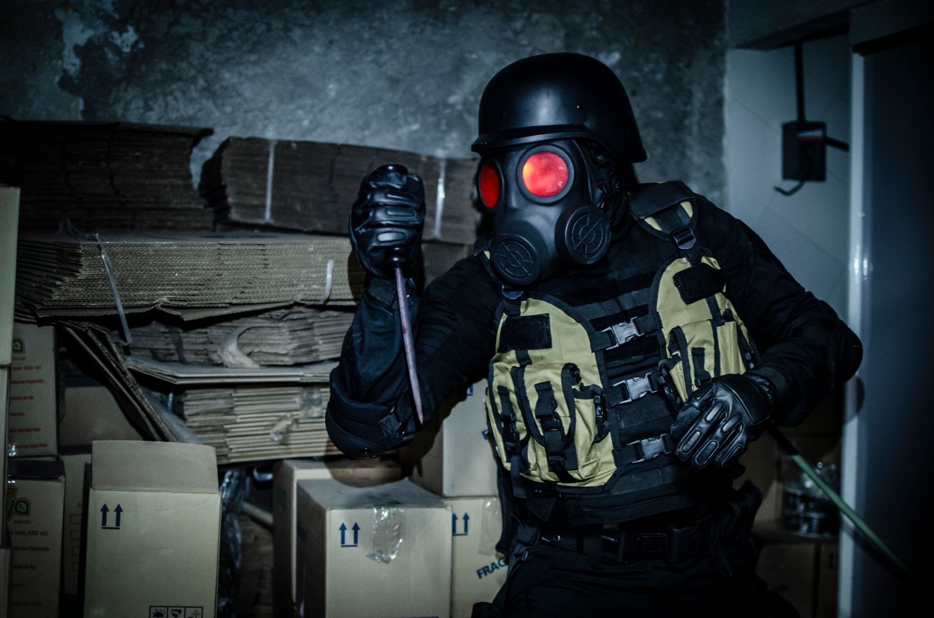 Individual in tactical gear and gas mask holding a weapon in an abandoned warehouse.
