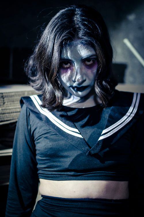 Free A woman with eerie Halloween makeup poses ominously in a dimly lit room, creating a haunting atmosphere. Stock Photo