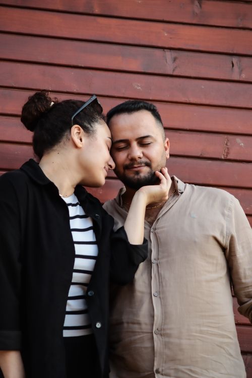 Free A couple shares an intimate moment leaning against a rustic wooden wall. Stock Photo