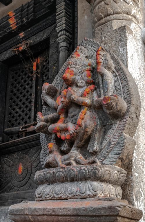 Free Ancient stone sculpture of a Hindu deity with vivid orange adornments. Stock Photo