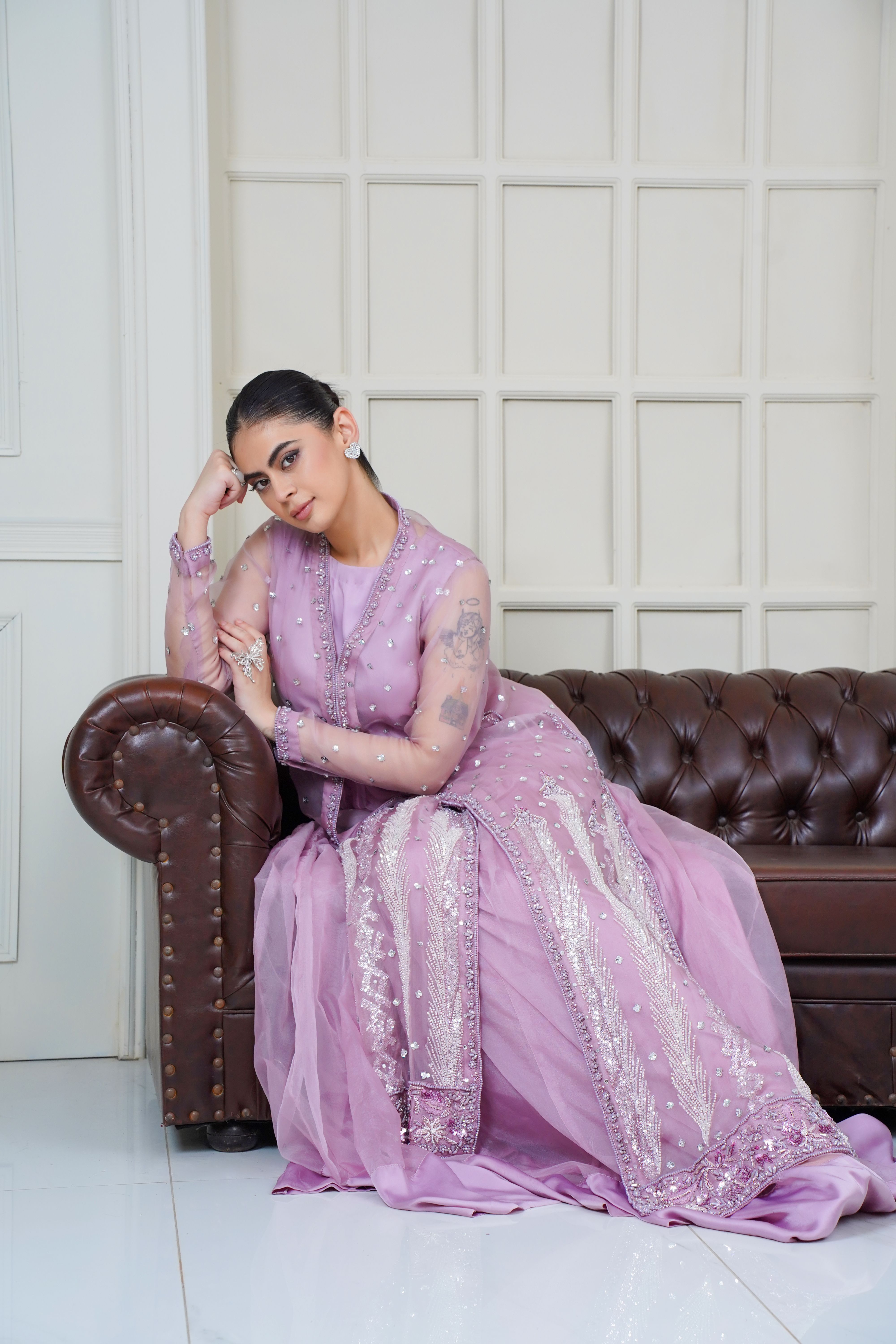 Chic portrait of a woman in a delicate lavender Eastern dress on a leather couch.