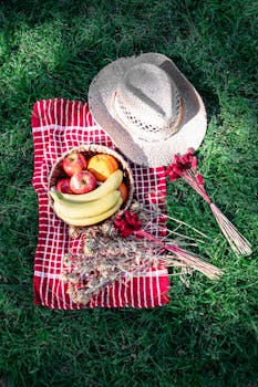 Vibrant picnic in a park with a variety of fruits and a cowboy hat on a red checkered blanket.