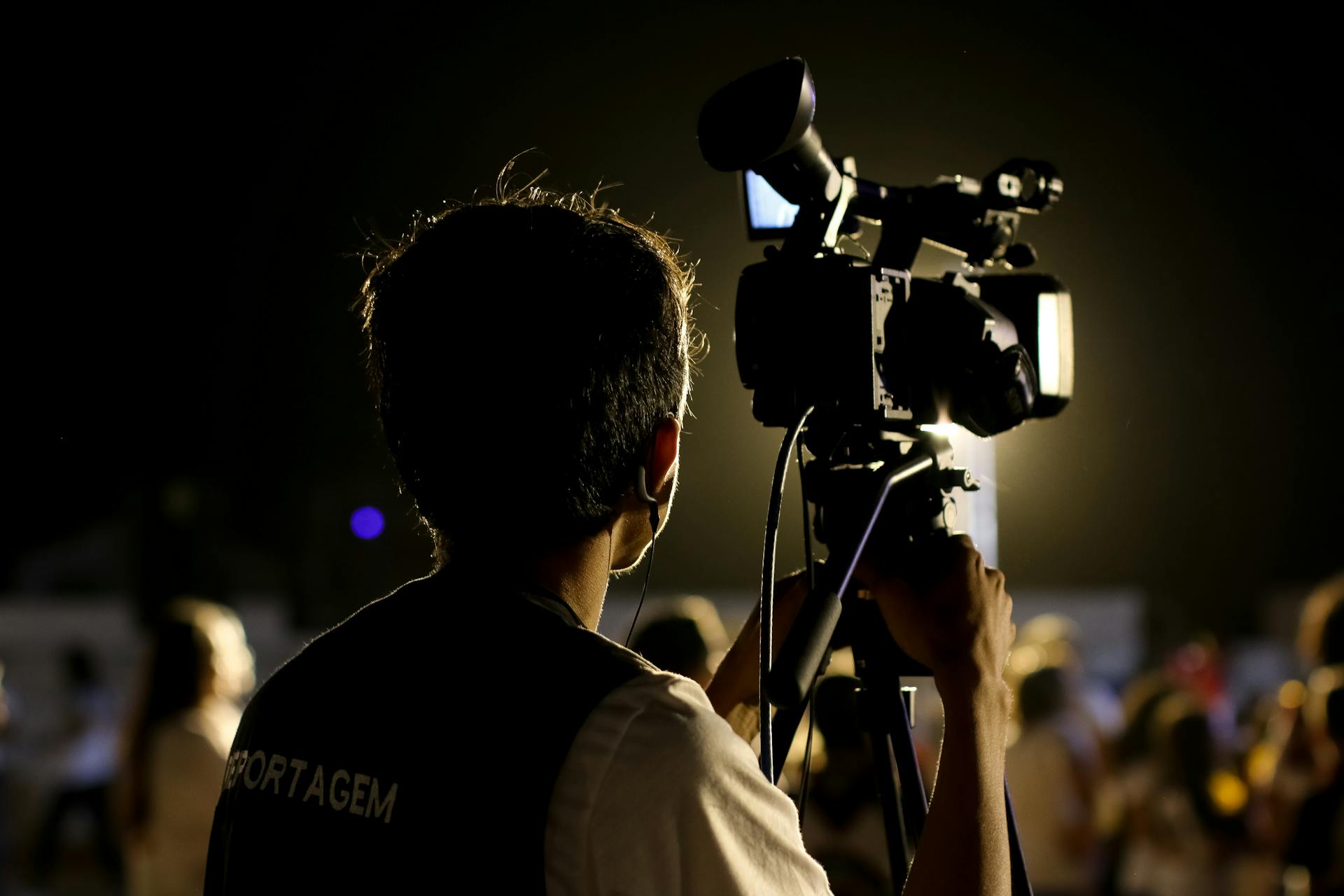 A cameraman filming an event outdoors at night with professional equipment, capturing the vibrant atmosphere.