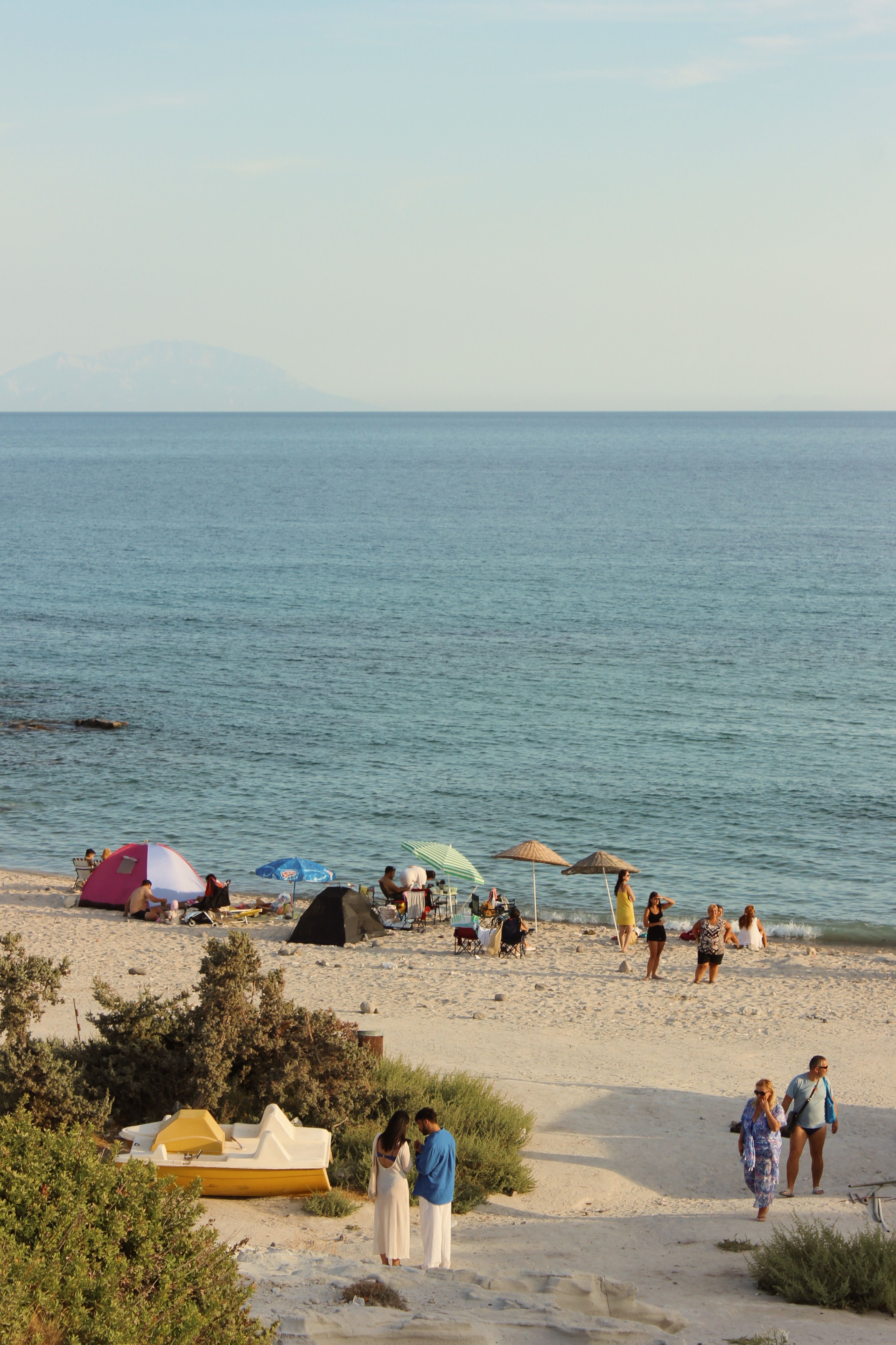 Peaceful beach scene with people, tents, and calm sea on a sunny day.