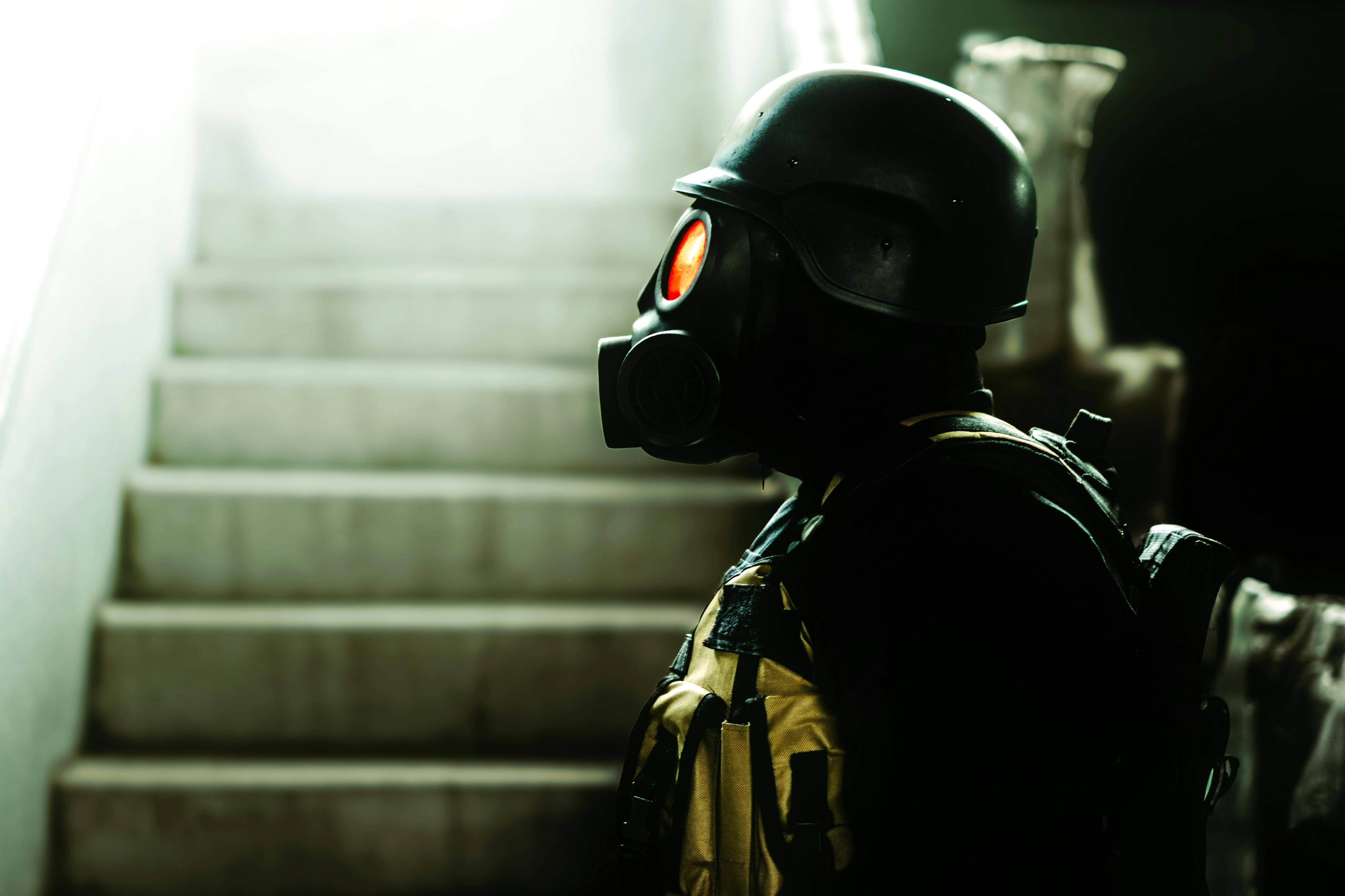 Dark indoor scene featuring a figure in gas mask and helmet, evoking horror and Halloween vibes.