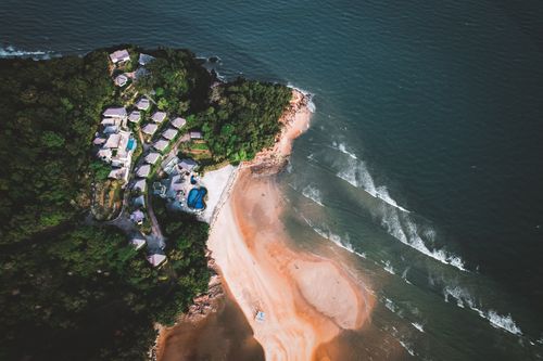 Free Stunning aerial view of a beachfront resort surrounded by lush greenery and coastal waters. Stock Photo