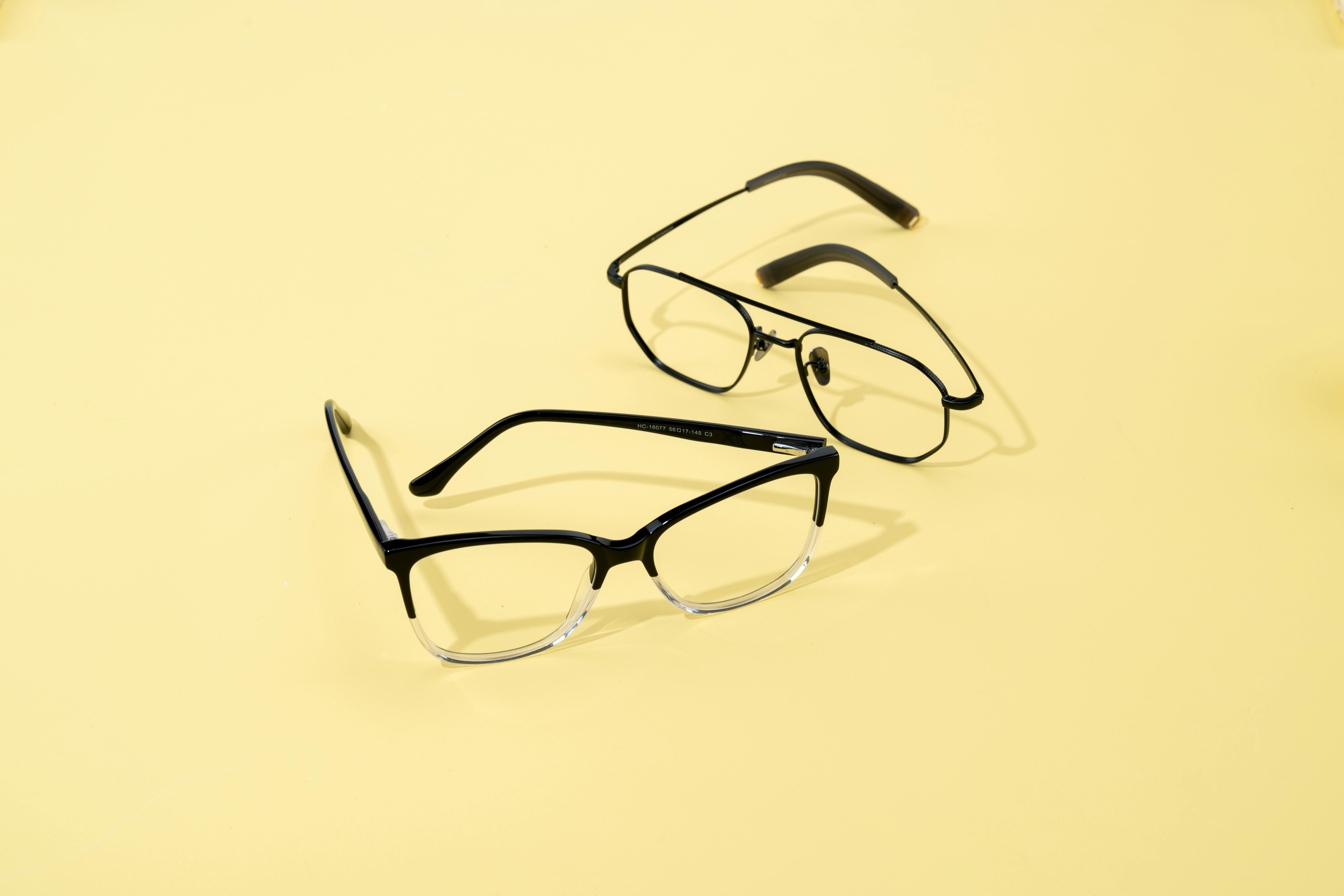 Two pairs of fashionable eyeglasses on a minimalist yellow backdrop.