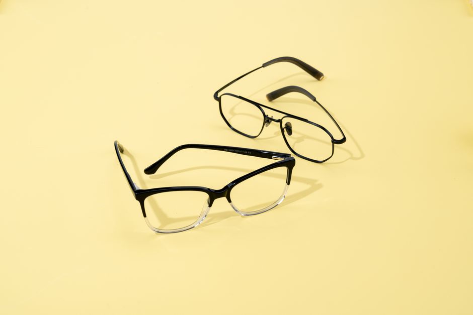 Two pairs of fashionable eyeglasses on a minimalist yellow backdrop.