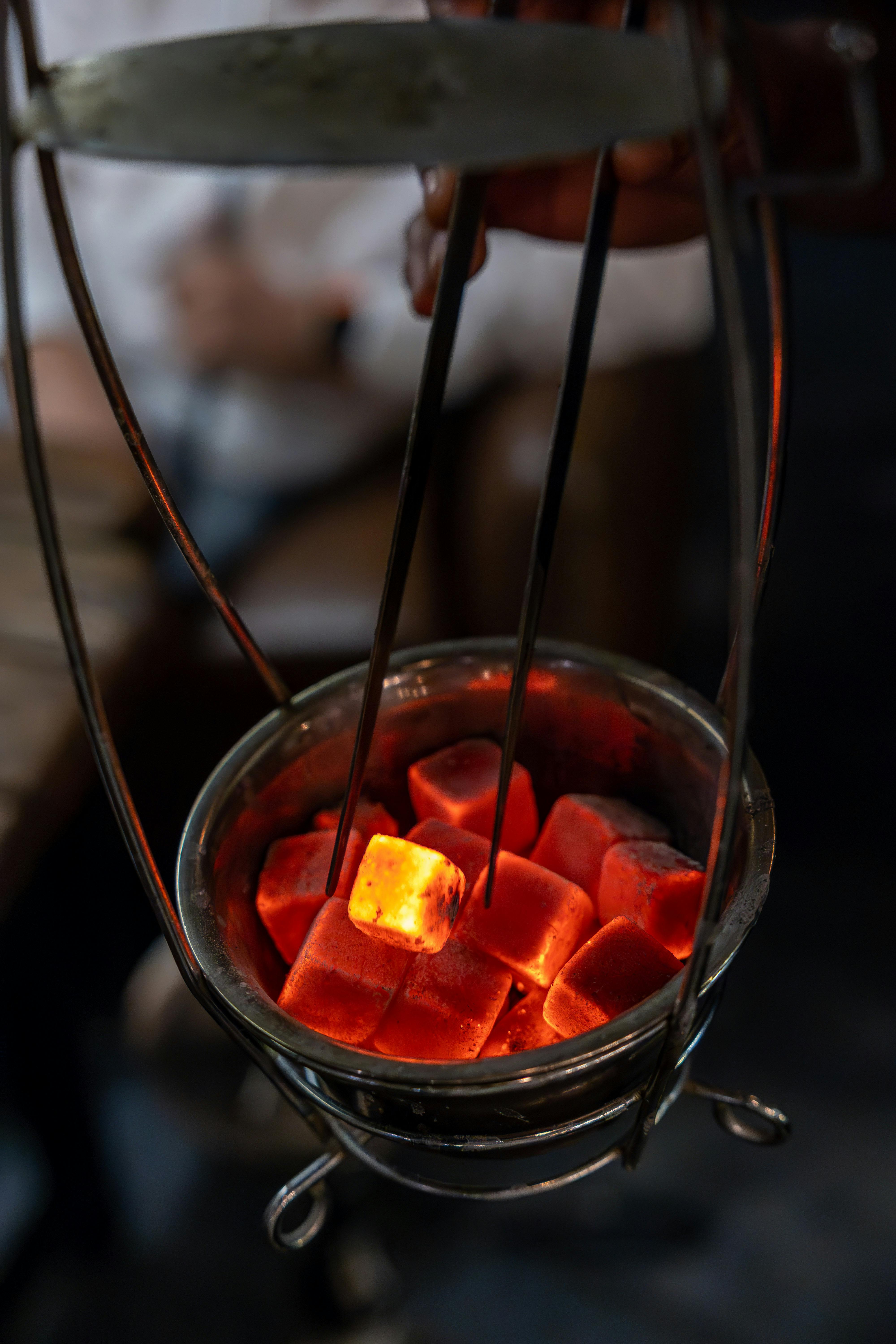 Close-up of glowing charcoal pieces in a metal holder with blurred background.
