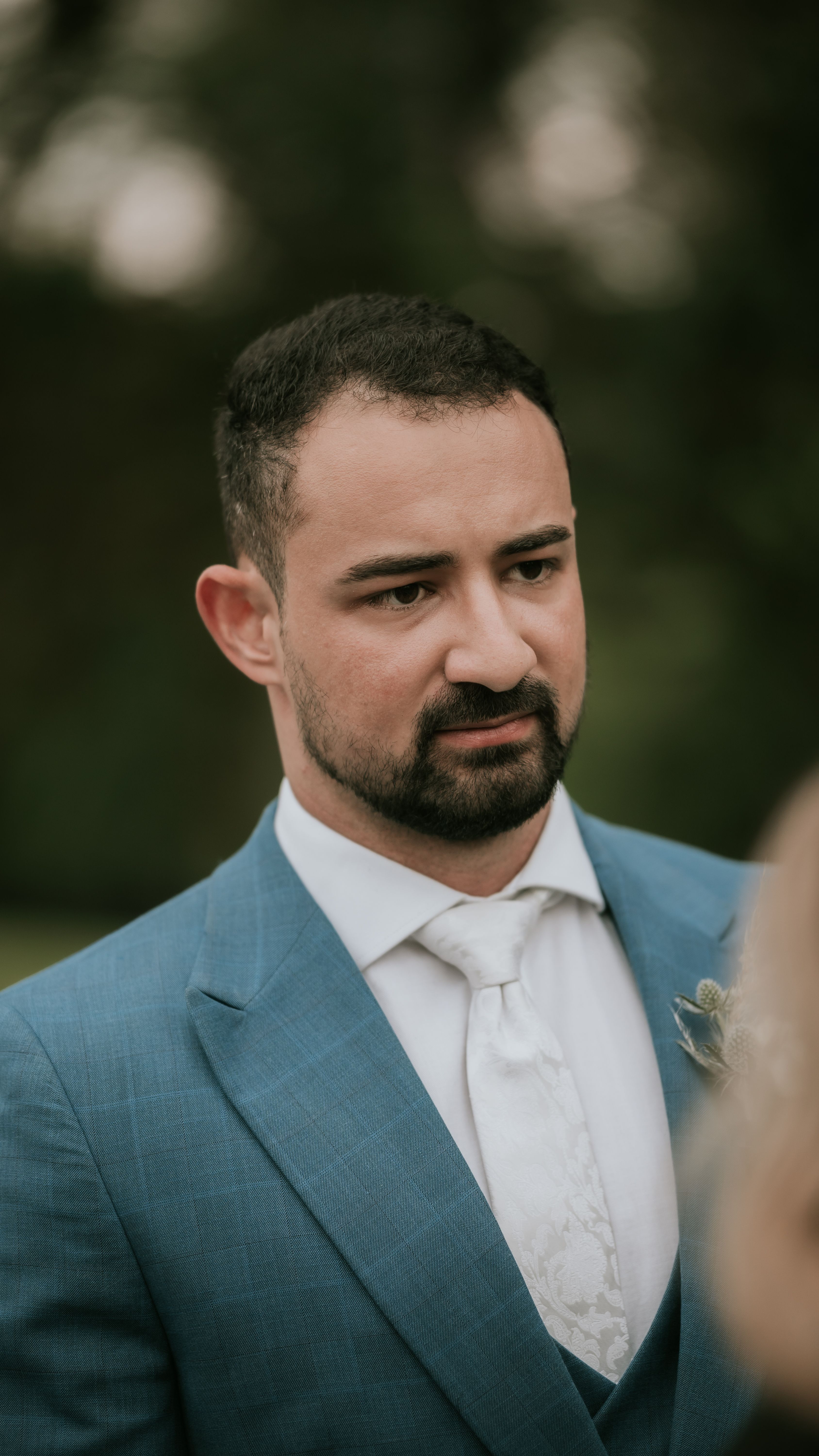 Close-up portrait of a man in a blue suit attending an outdoor event, conveying a sense of elegance and sophistication.