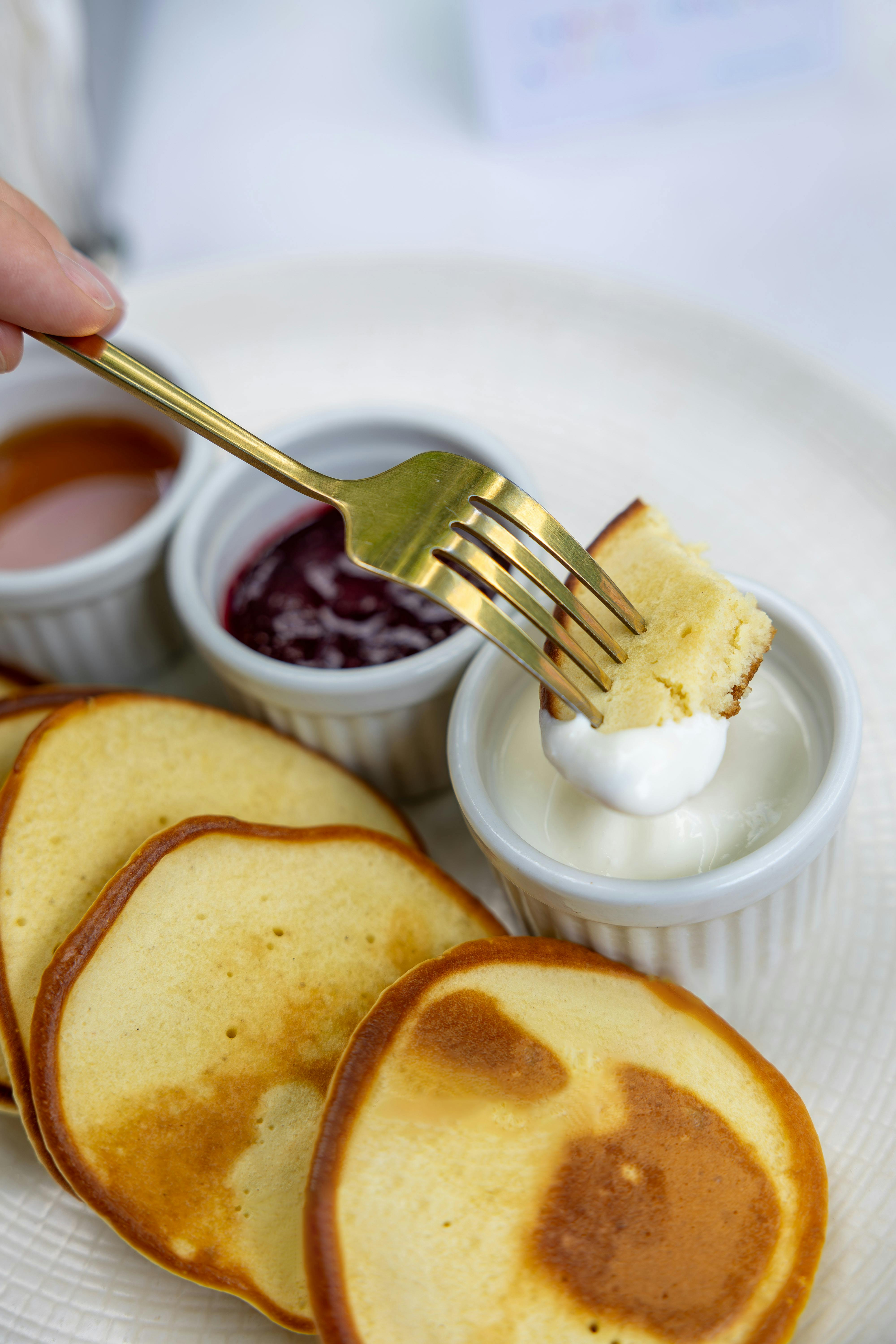 Close-up of pancakes with jam, syrup, and sour cream on a plate for a delightful breakfast.