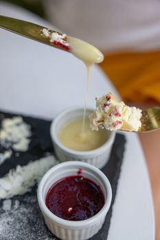 Close-up view of cheesecake with fruit jam and condensed milk on a slate plate.