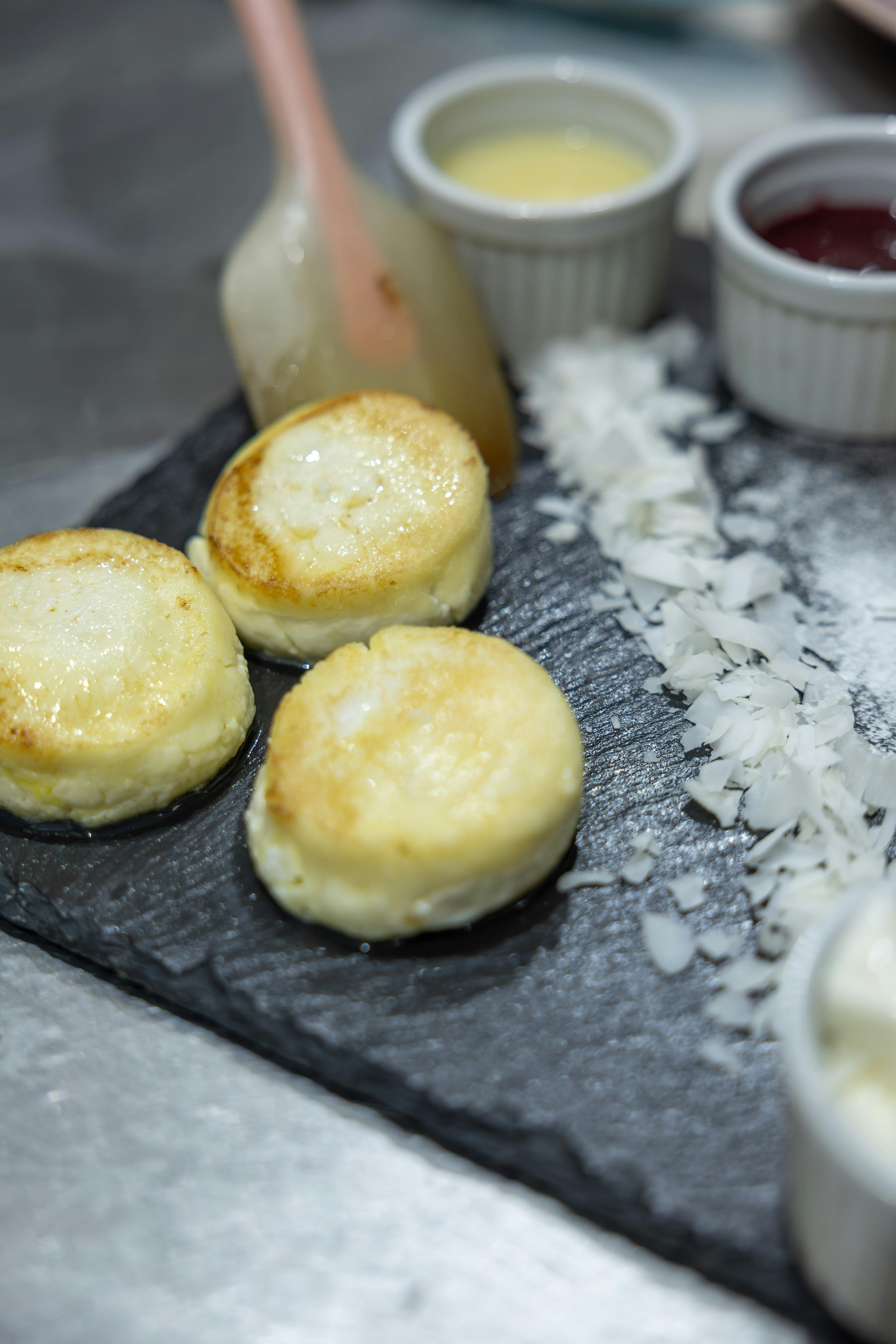 Close-up of homemade syrniki served with various condiments on a slate board.
