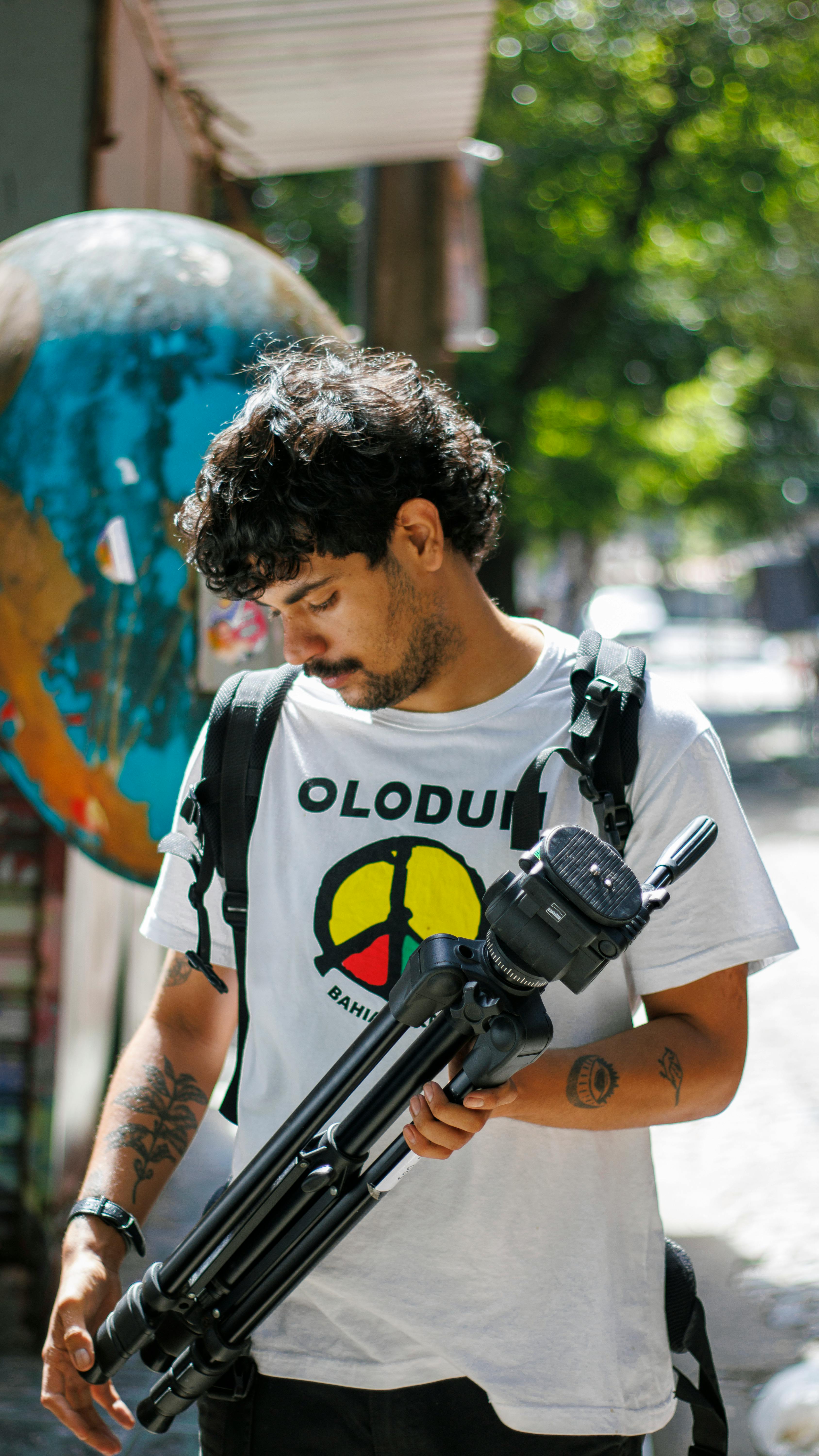 Man holding tripod on city street with globe art in background.