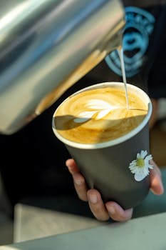 A barista pours a beautiful latte art into a cup, showcasing coffee craftsmanship.
