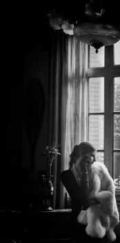 A dramatic black and white portrait of an elegant woman near a window.