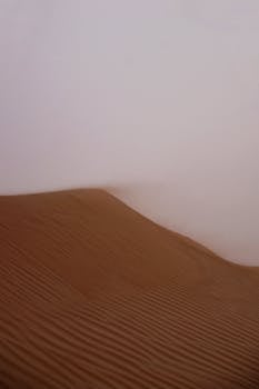 晴朗的天空下，广阔的沙漠中，沙丘被沙尘暴笼罩