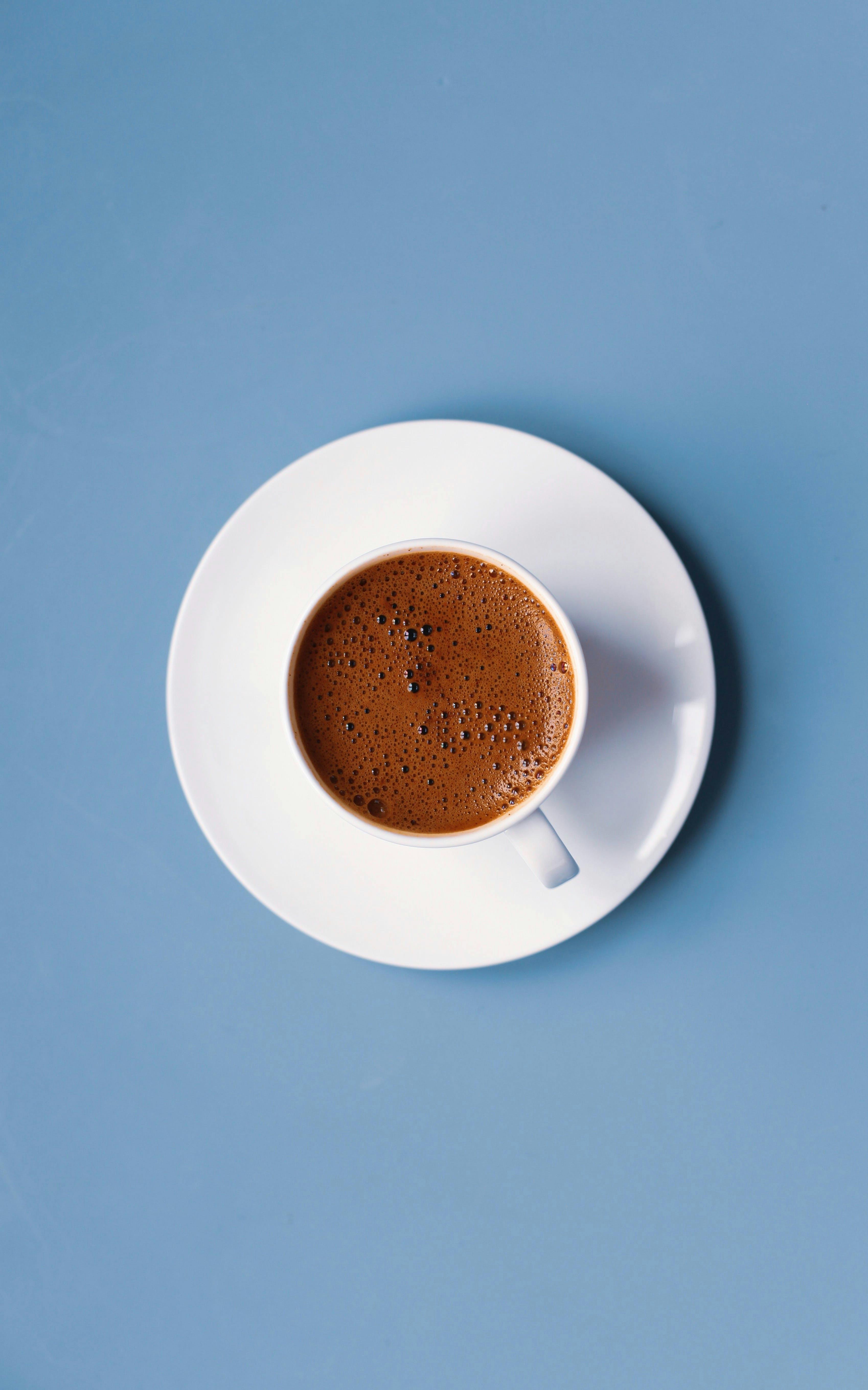 A delicate cup of Italian espresso on a white saucer set against a serene blue background.
