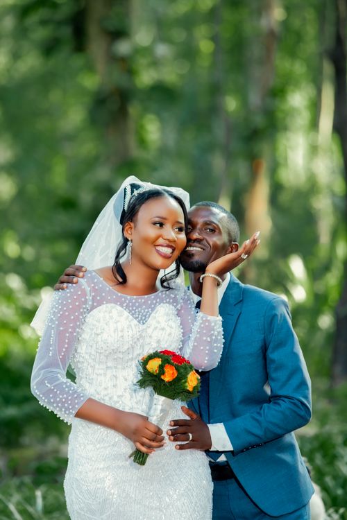 Free Happy bride and groom posing outdoors in wedding attire, surrounded by vibrant greenery. Stock Photo