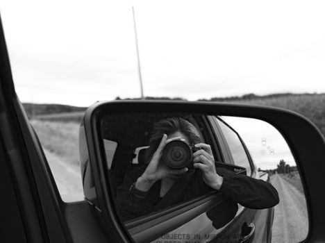 Black and white photo of a photographer taking a picture in a car side mirror.