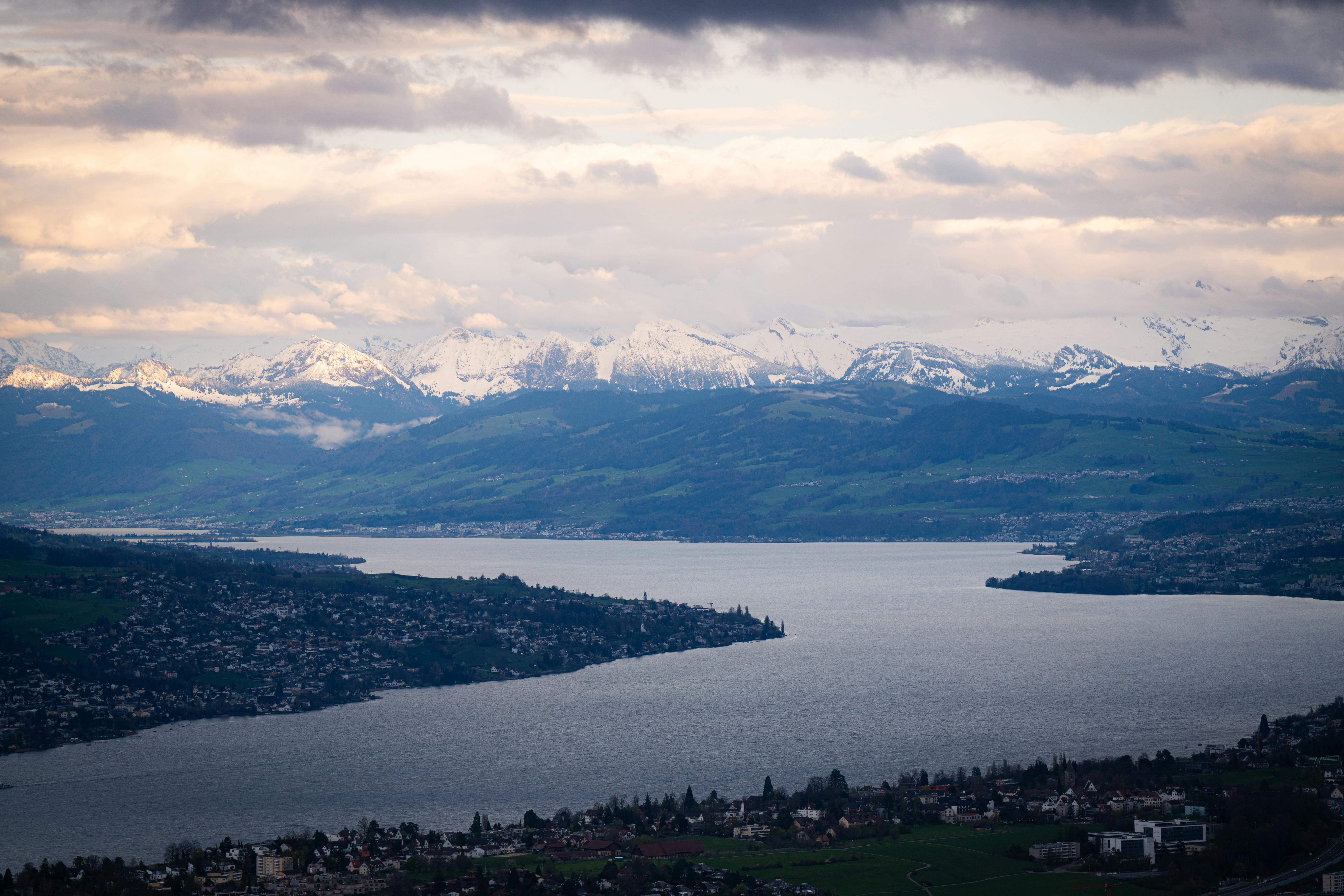 A breathtaking view of the snowy Alps and a tranquil lake under a dramatic twilight sky.