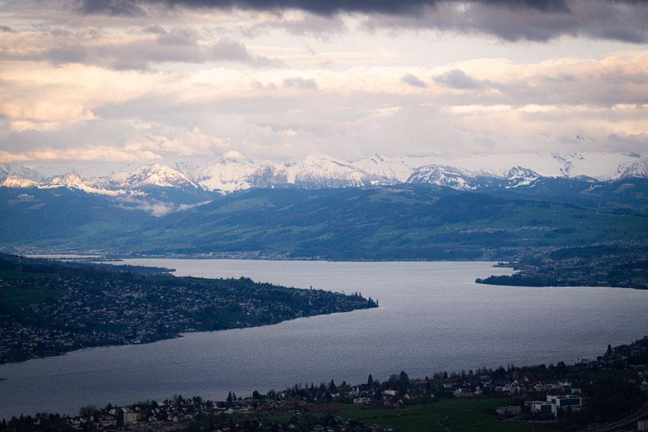 A breathtaking view of the snowy Alps and a tranquil lake under a dramatic twilight sky.
