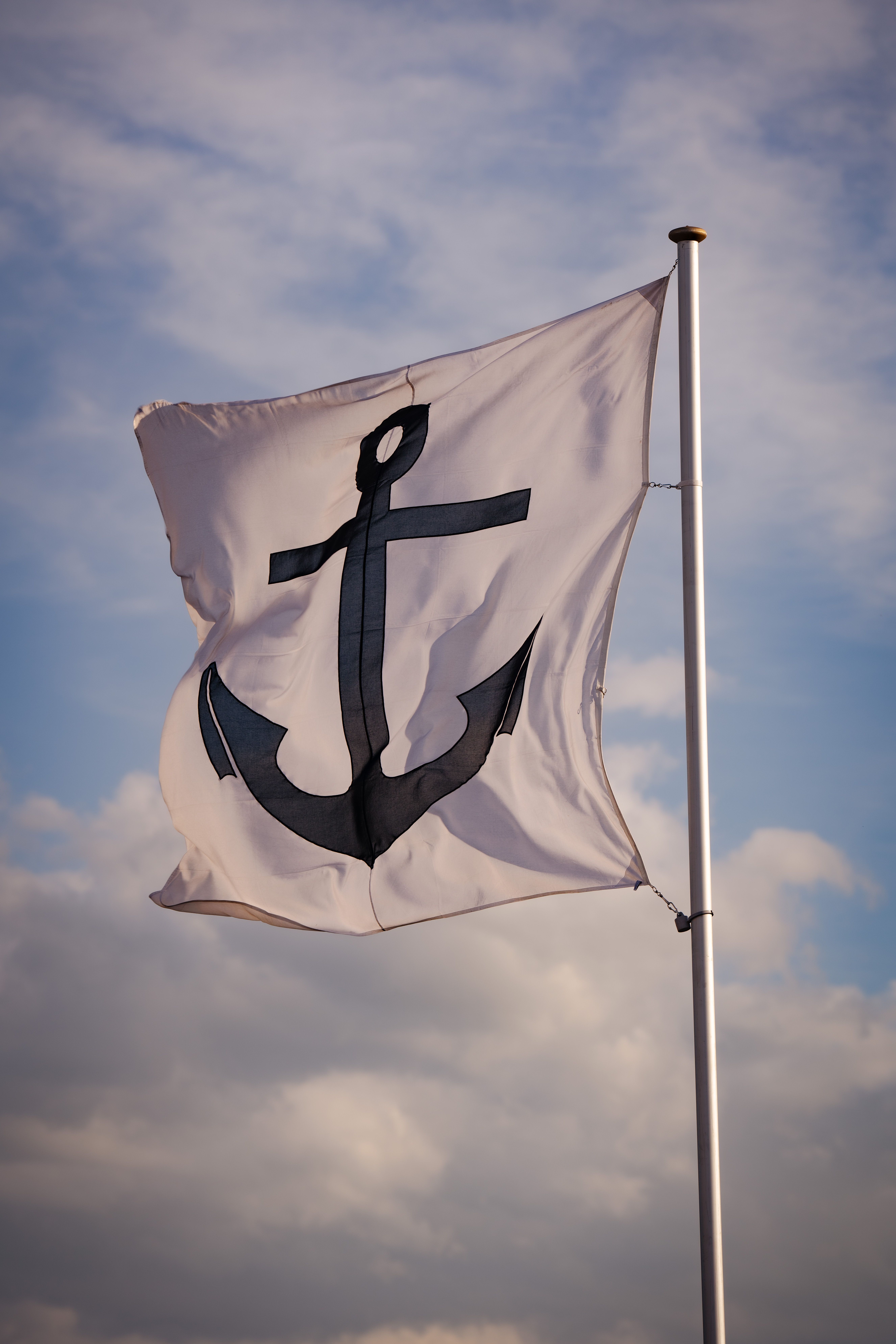 A white flag with a black anchor symbol waving against a clear sky, symbolizing nautical themes.
