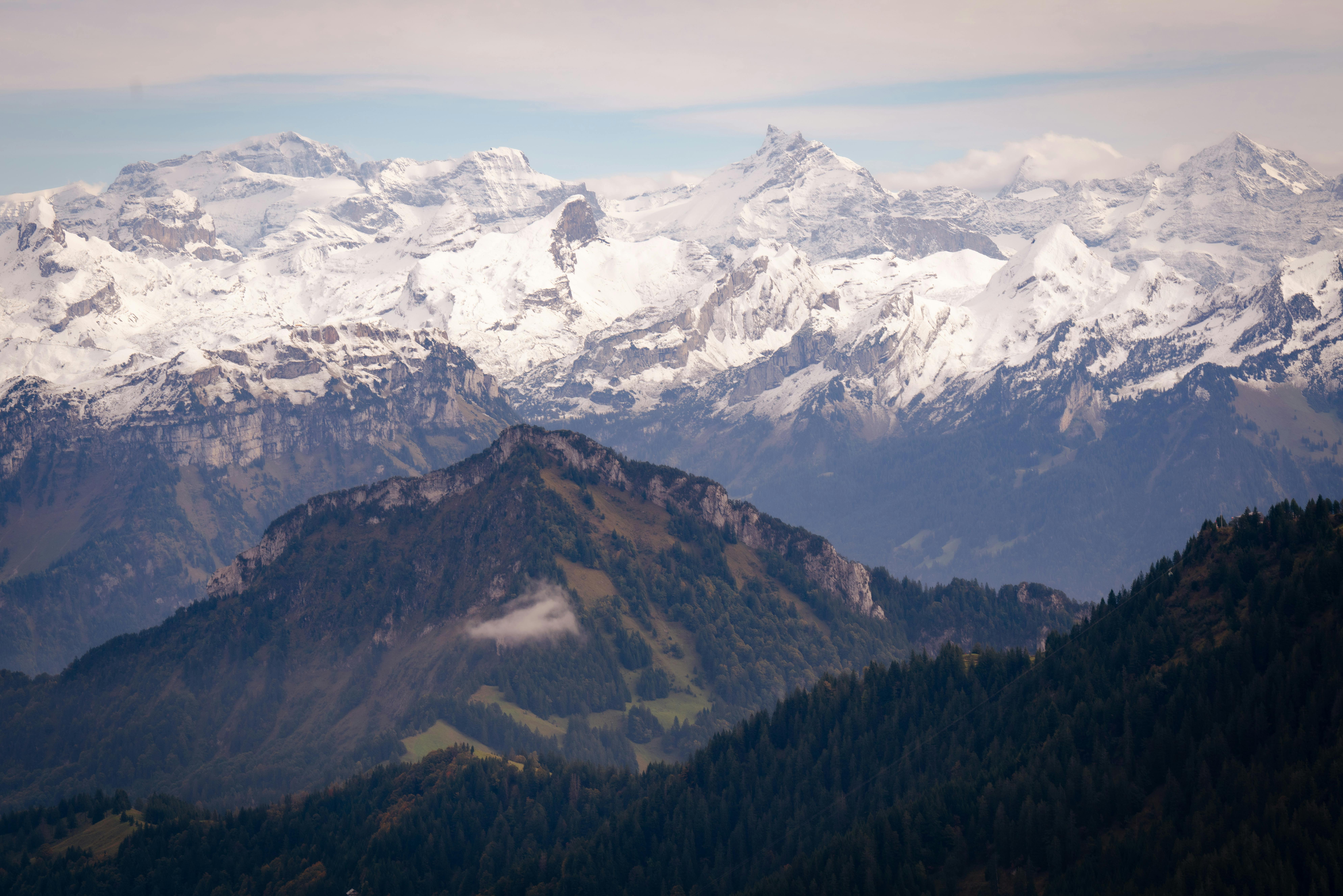 Prescription Goggle Inserts - Breathtaking panoramic view of a snow-capped mountain range with layers of lush forests in the foreground.