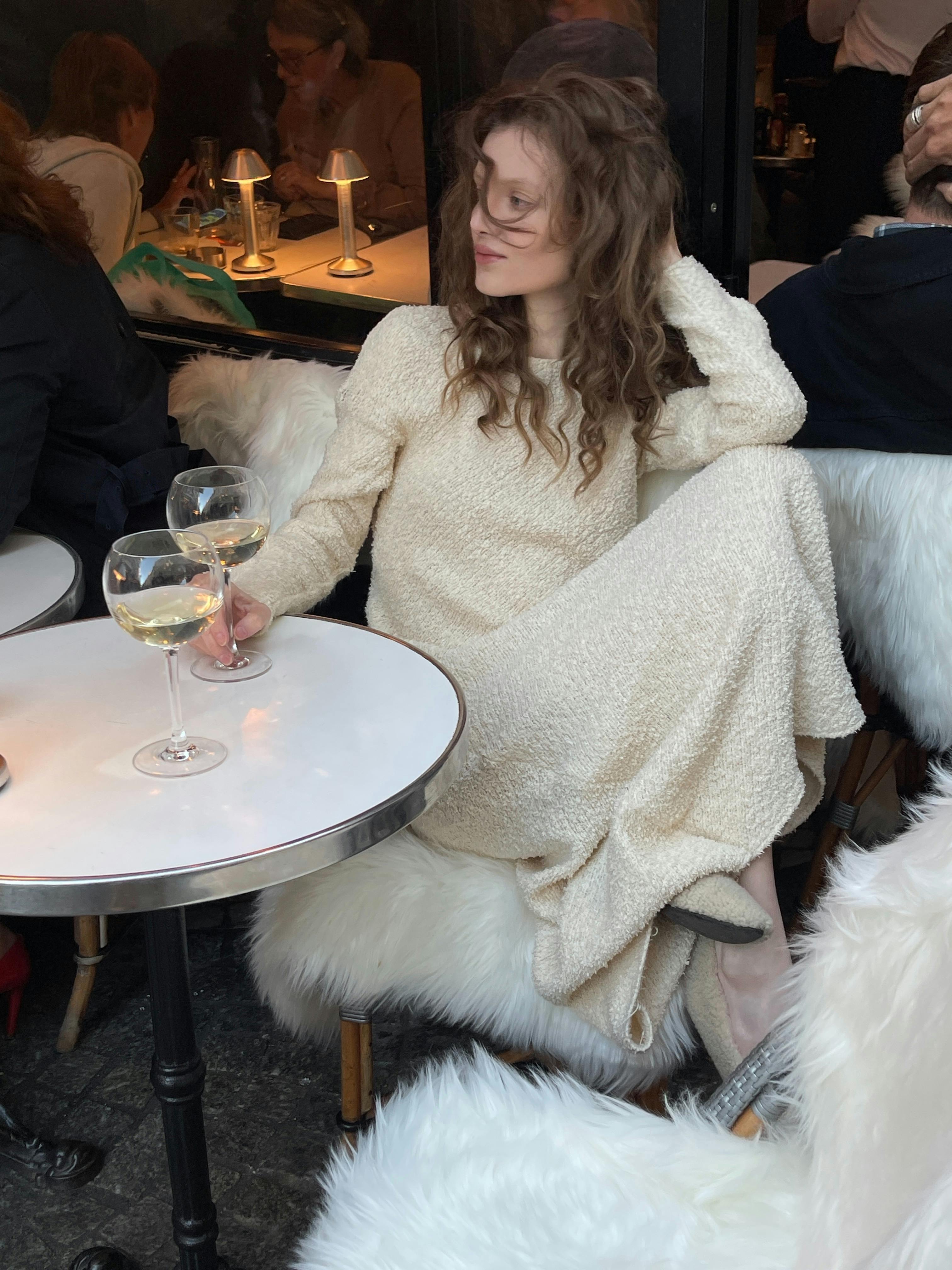 Stylish woman in cream coat enjoying wine at a cozy café setting.