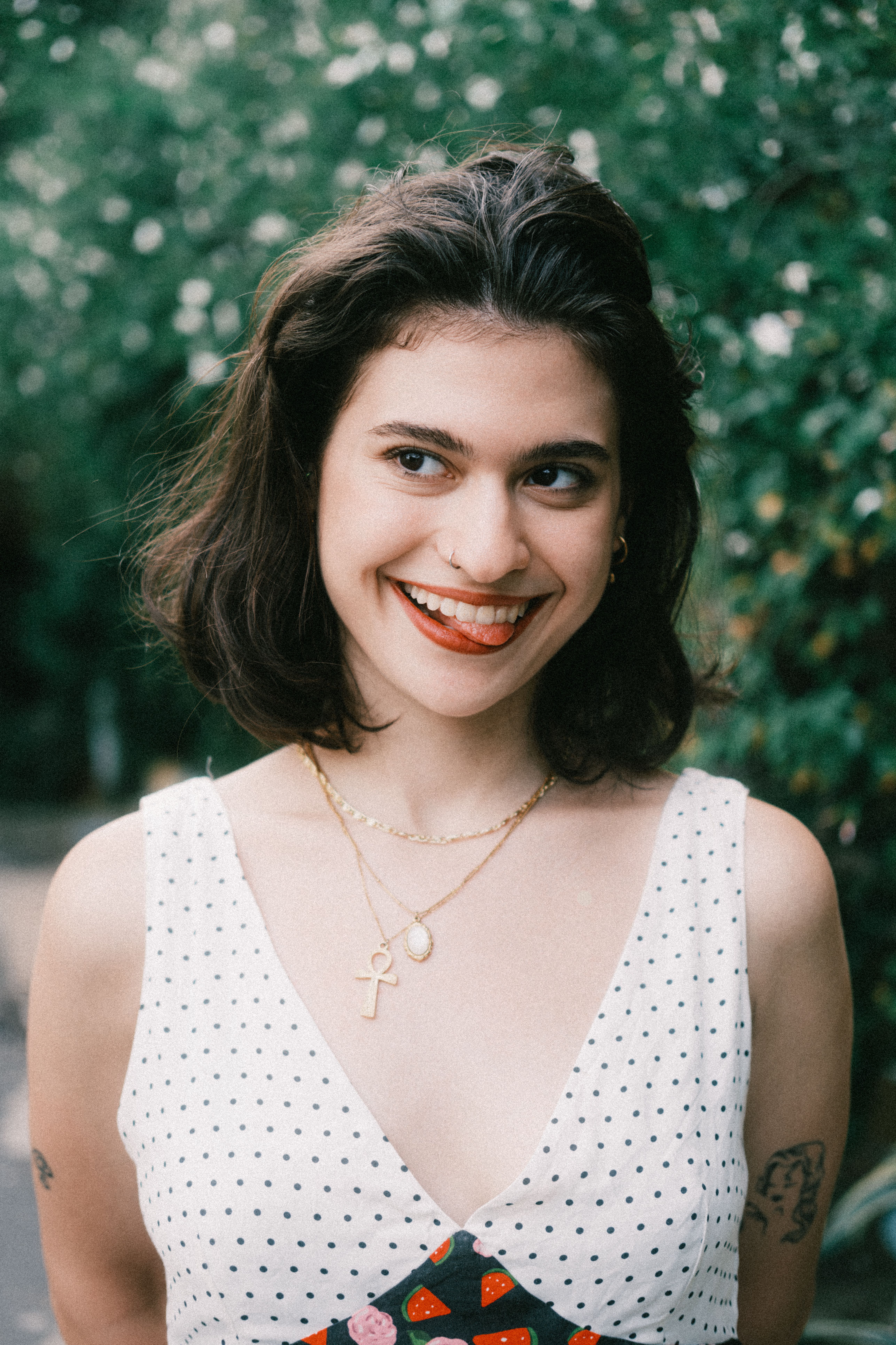Young woman smiling in a polka dot dress with a lush green background.