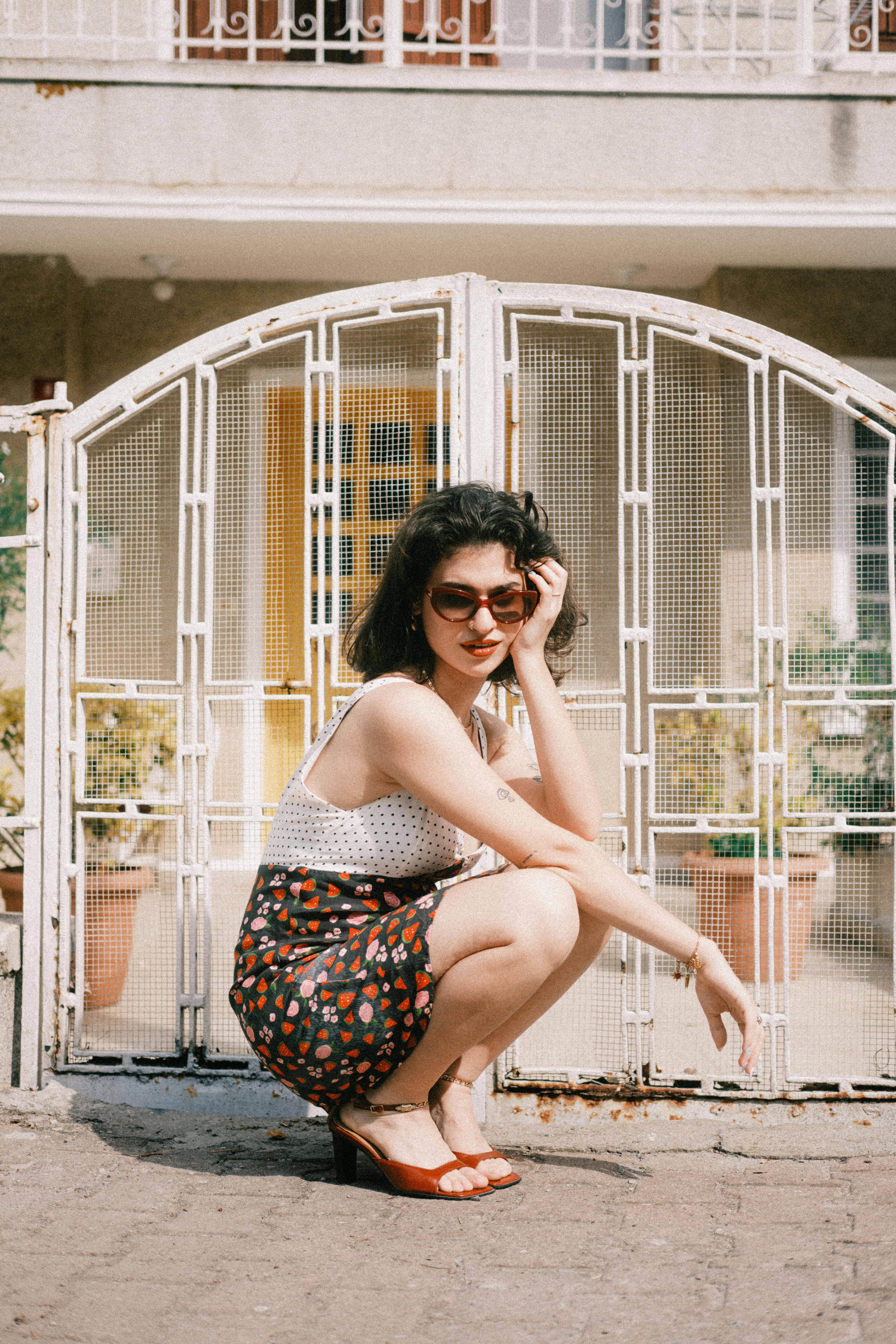 Trendy woman squatting stylishly by a decorative gate in daylight.
