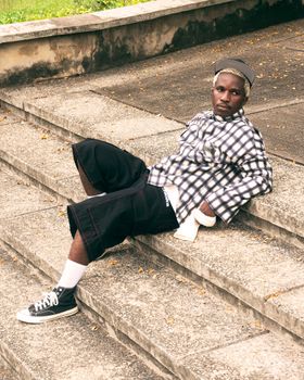 Casually dressed young man resting on stone steps outdoors in a relaxed pose.