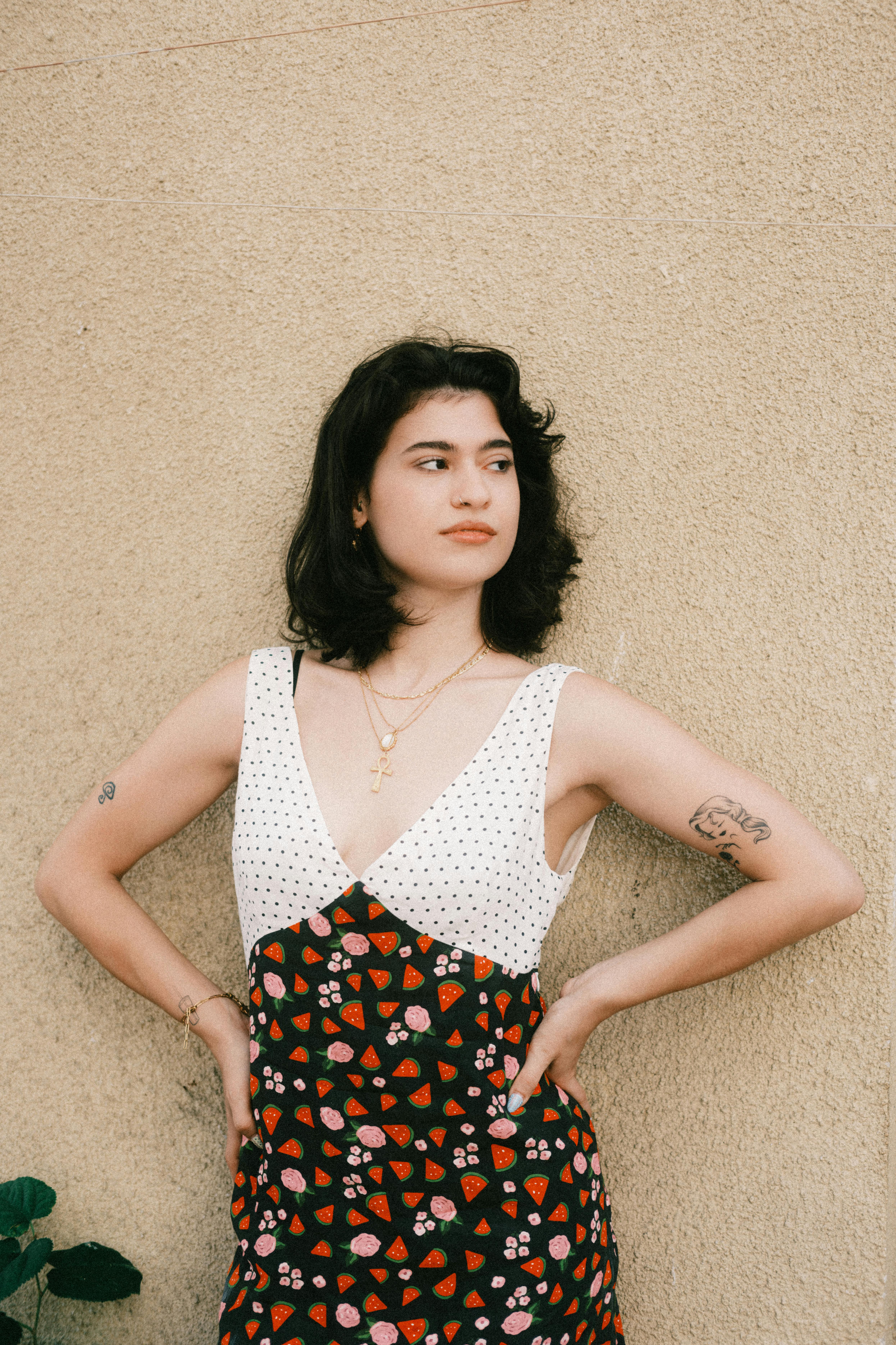 Portrait of a young woman in a patterned dress against a textured wall outdoors.