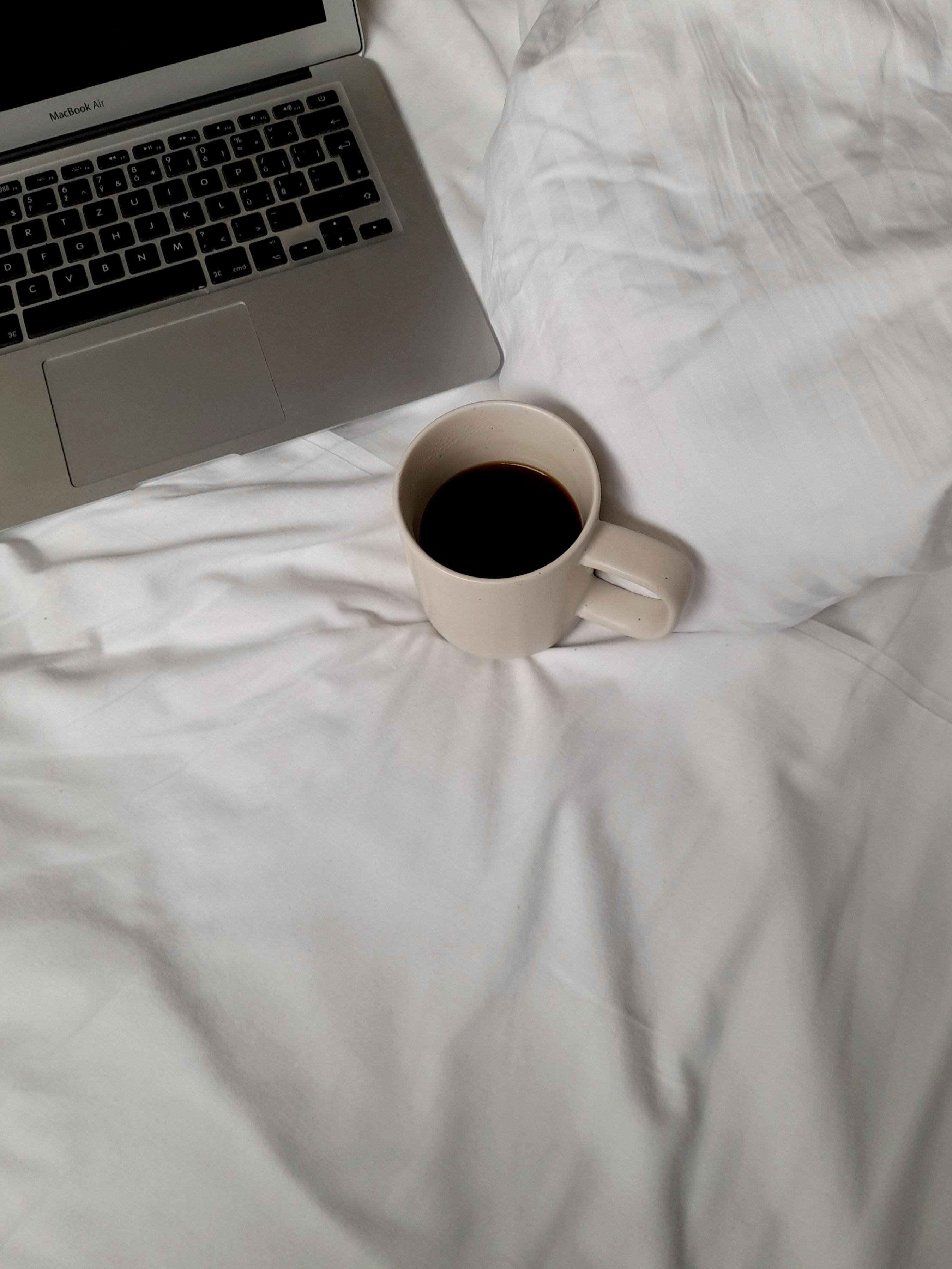 A calming morning scene with a laptop and coffee cup on a white bedspread, perfect for remote work vibes.