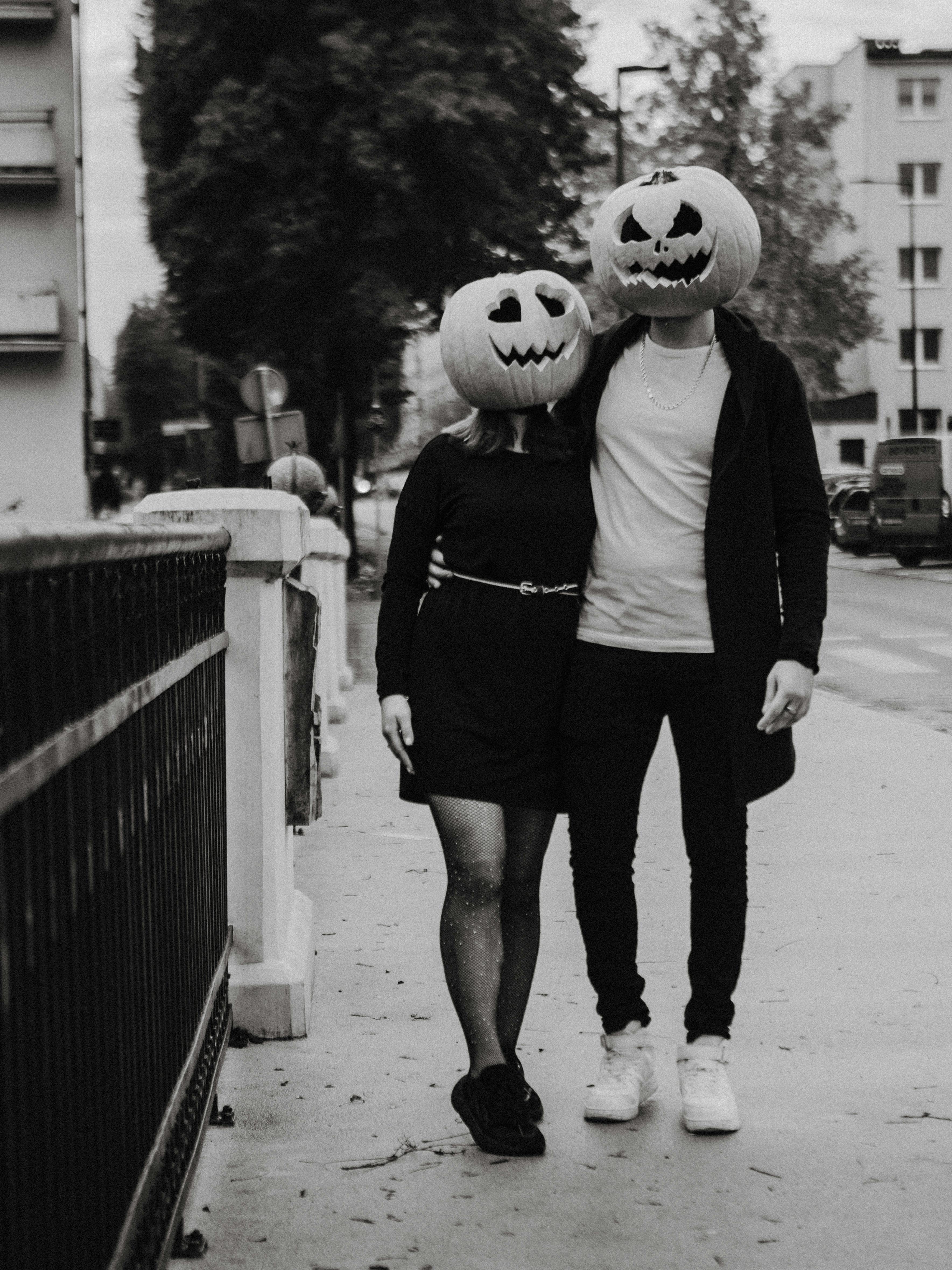 A couple wears carved pumpkin heads in a Halloween-themed street scene.
