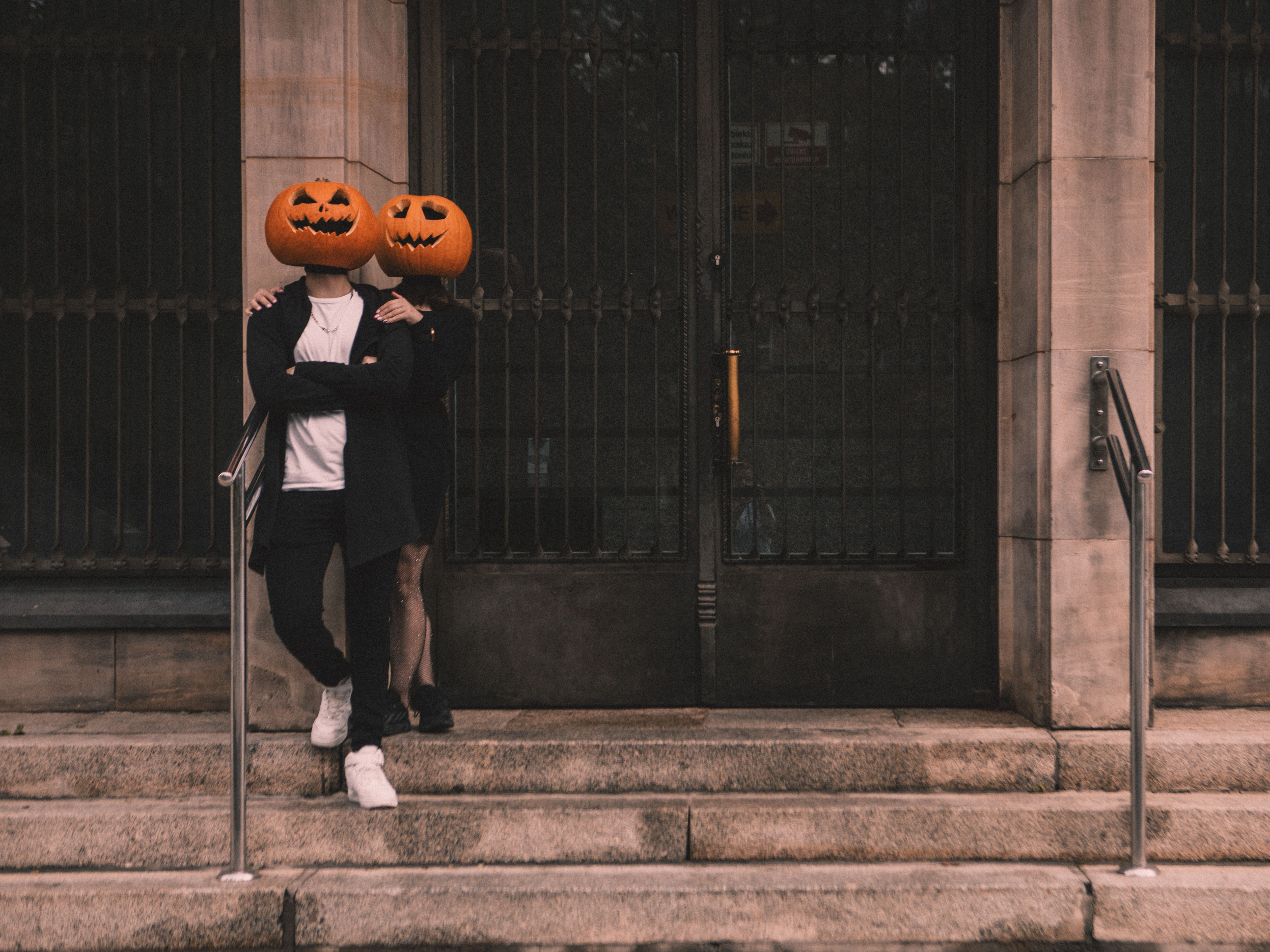 Couple wearing pumpkin head costumes embracing on a stone staircase.