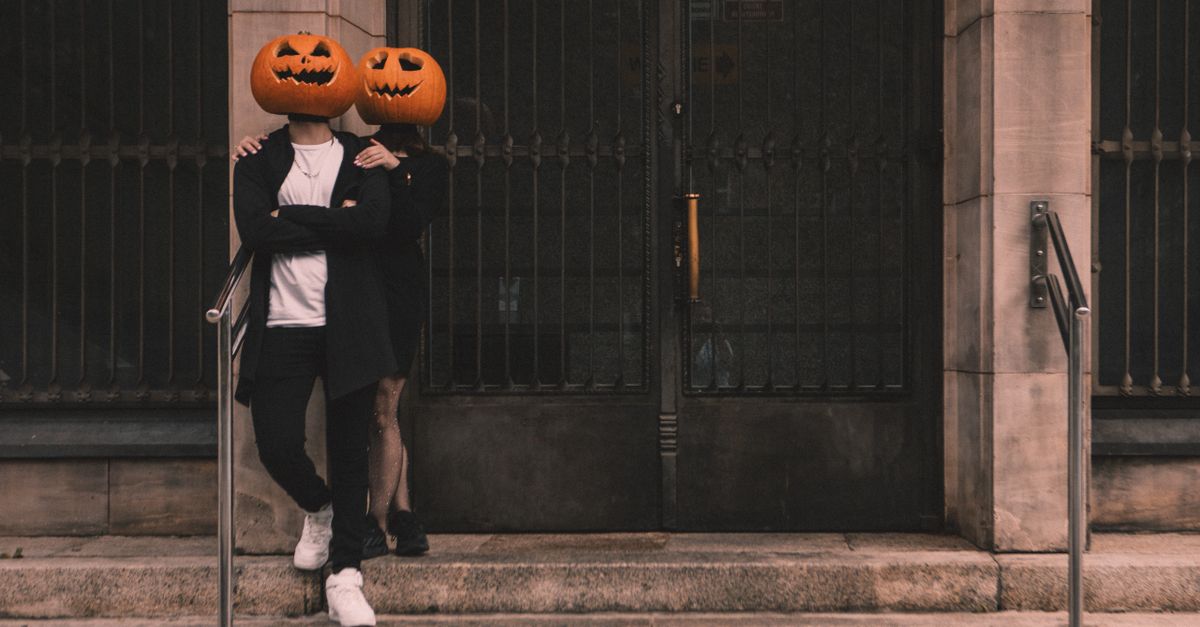Couple wearing pumpkin head costumes embracing on a stone staircase.
