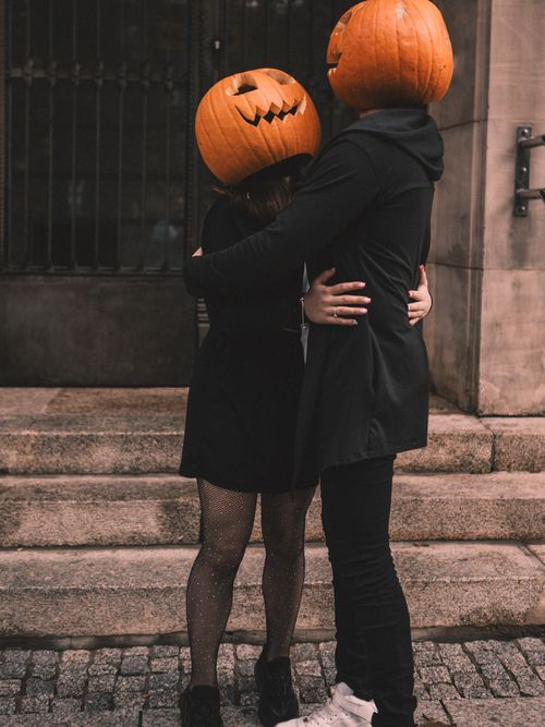 Free A couple wearing pumpkin masks embraces on urban steps, capturing a playful Halloween moment. Stock Photo