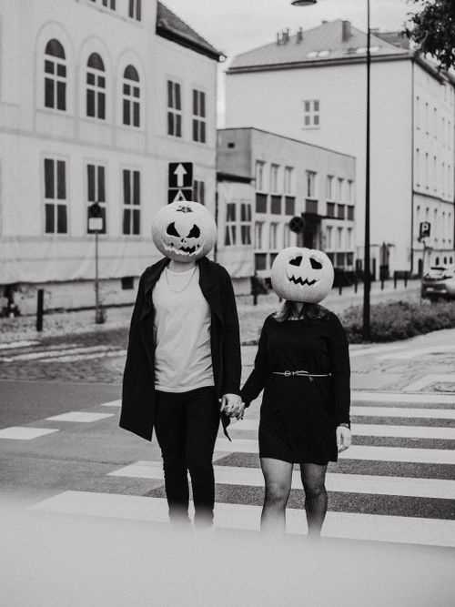 Free A couple with pumpkin heads crossing a street, capturing a whimsical Halloween vibe in black and white. Stock Photo