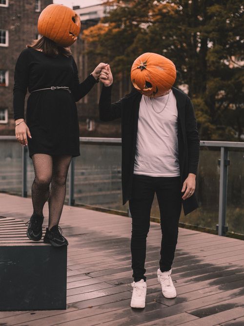 Free Couple with pumpkin heads holding hands outdoors, capturing Halloween spirit. Stock Photo