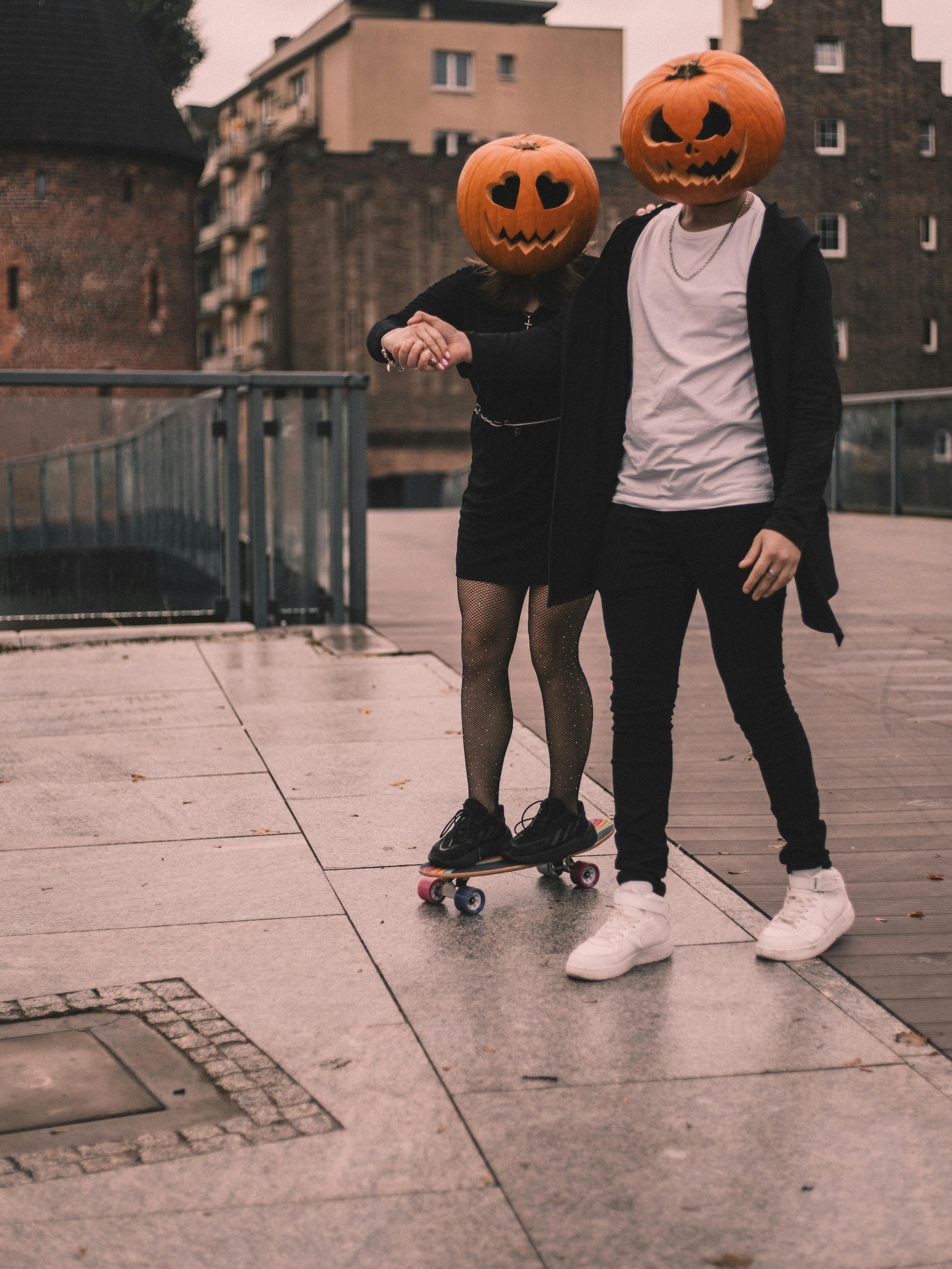 Free Two people with pumpkin masks skateboard outdoors, embodying Halloween spirit. Stock Photo