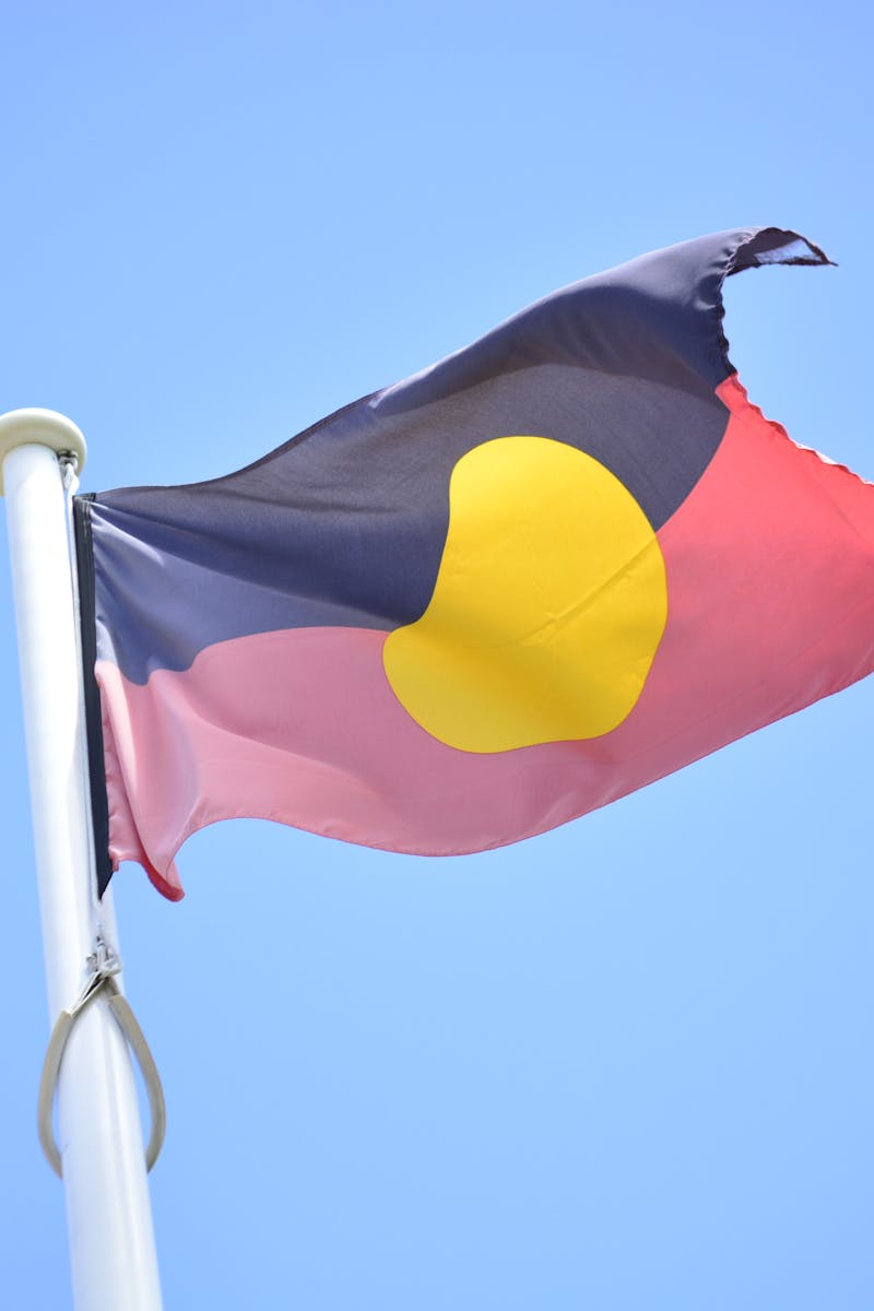 Australian Aboriginal flag waving against a clear blue sky, symbolizing culture and heritage.