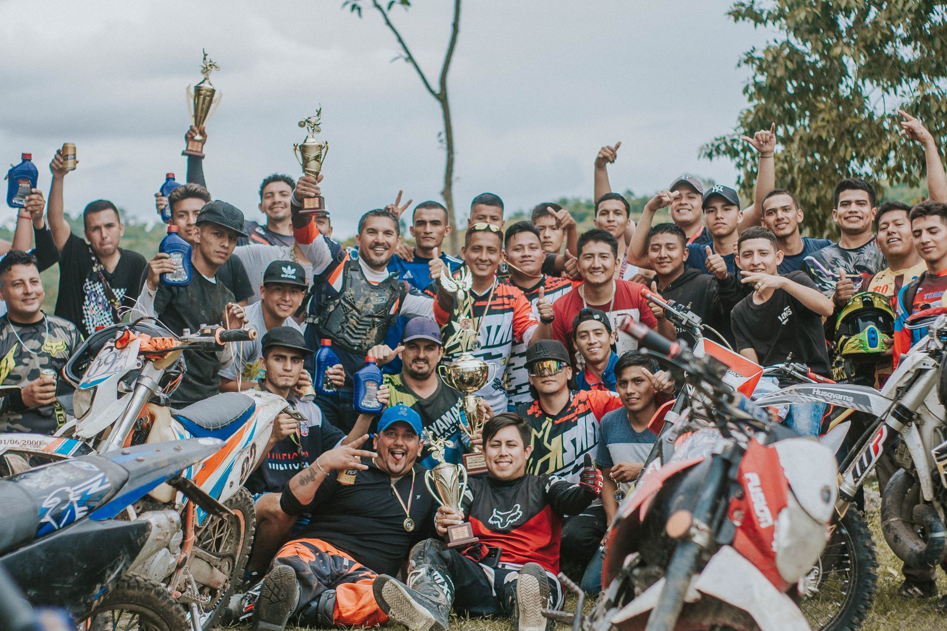 Motocross riders celebrate with trophies and drinks during a sunny outdoor event.