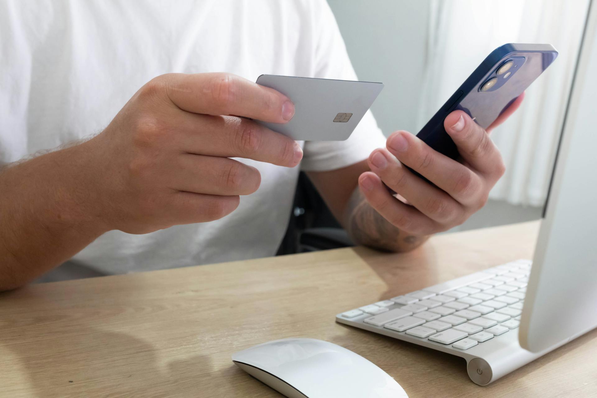 Person holding credit card and smartphone for an online transaction at a desk.