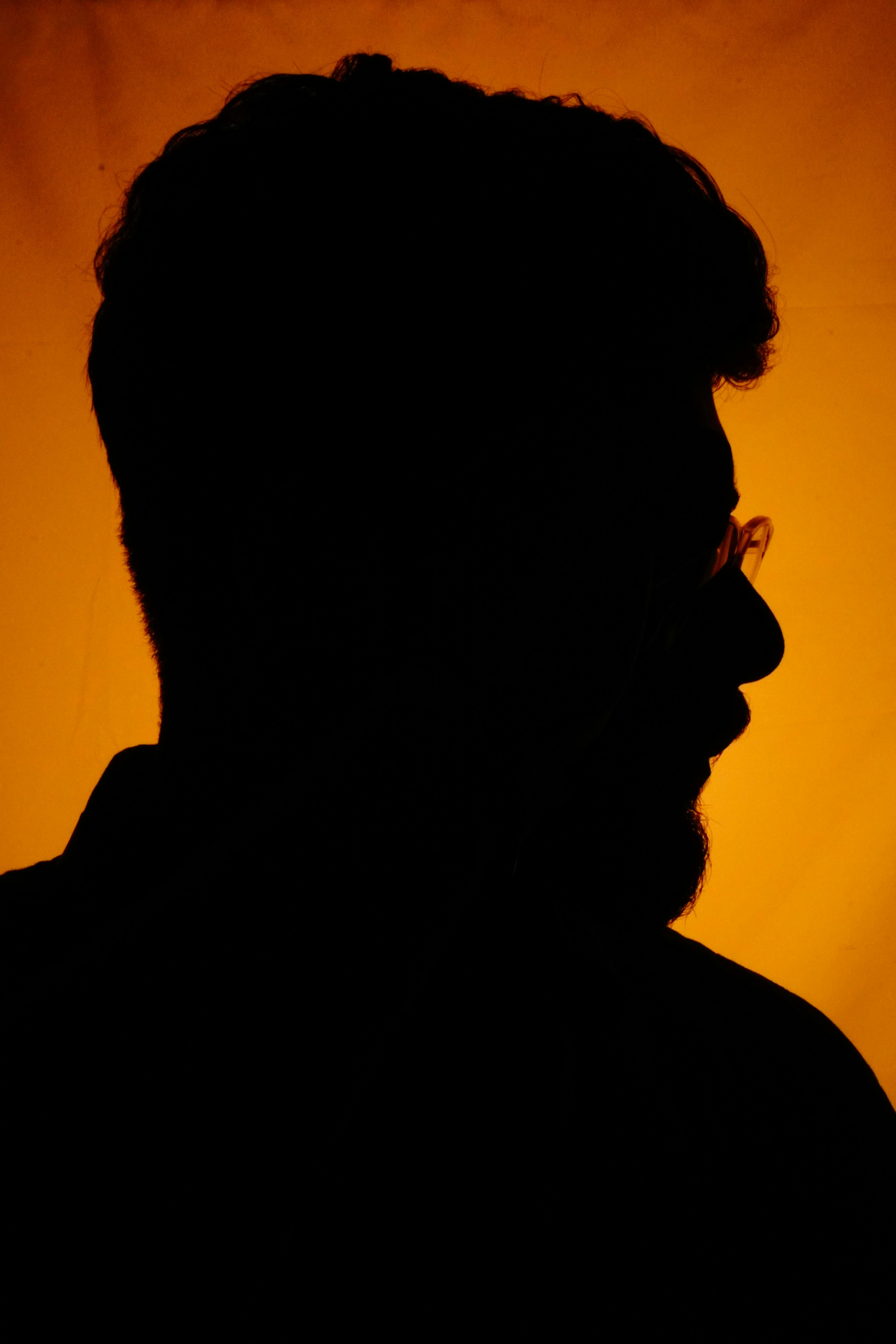 Dramatic silhouette of a man's profile with an amber background, conveying mystery and depth.