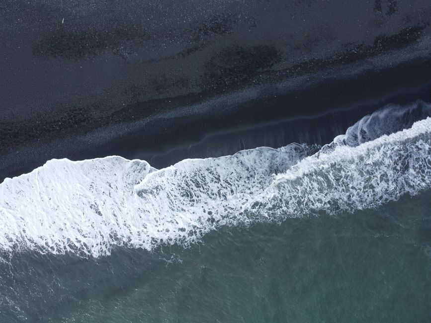 Dramatic aerial shot of ocean waves crashing onto a black sand beach in Iceland.
