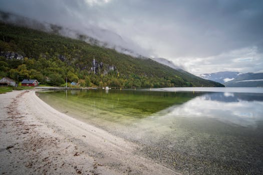 Tranquil fjord with mountains and cloudy sky in Norway, reflecting in calm waters.