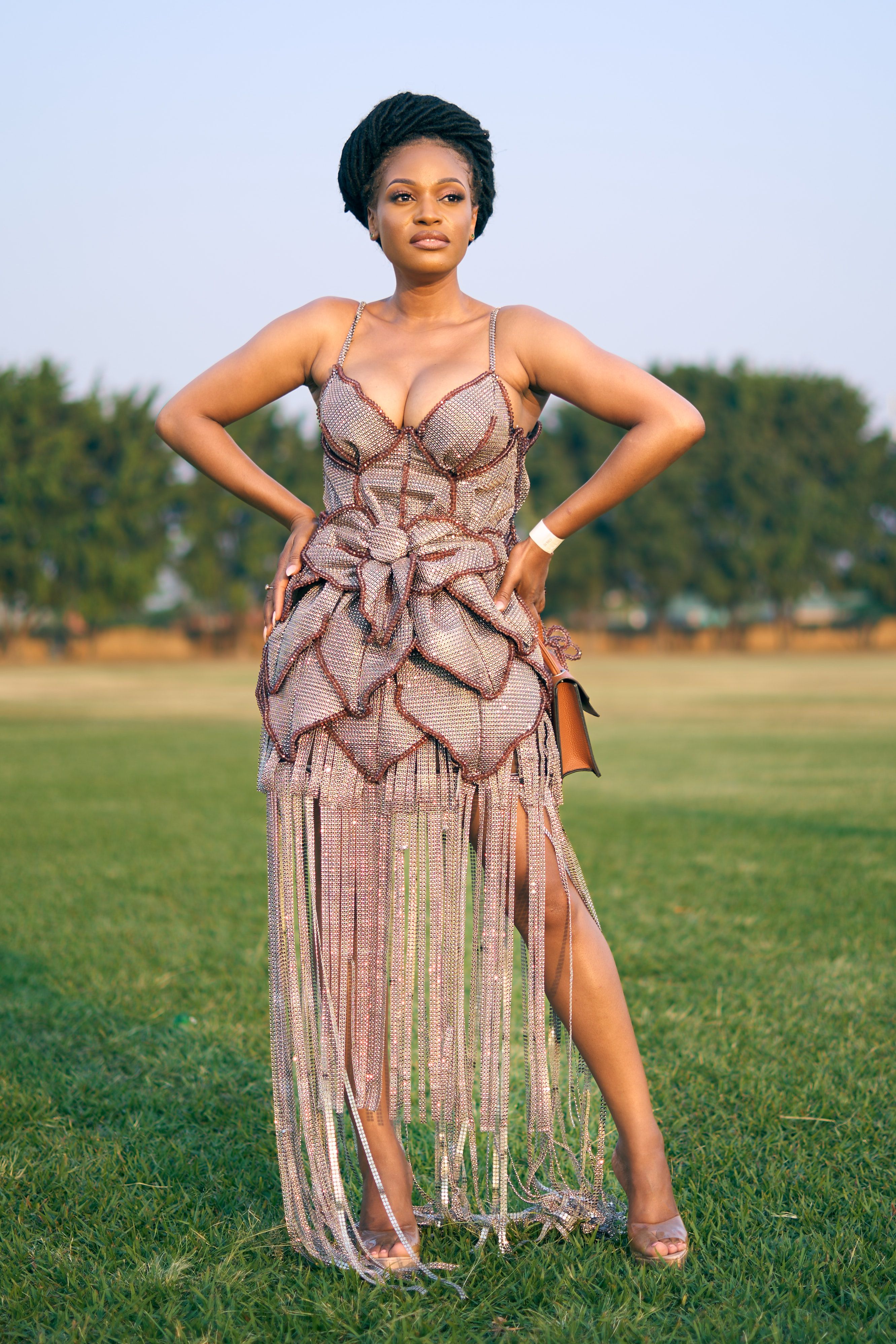 A stylish woman poses confidently outdoors in a chic dress, embodying elegance and strength.