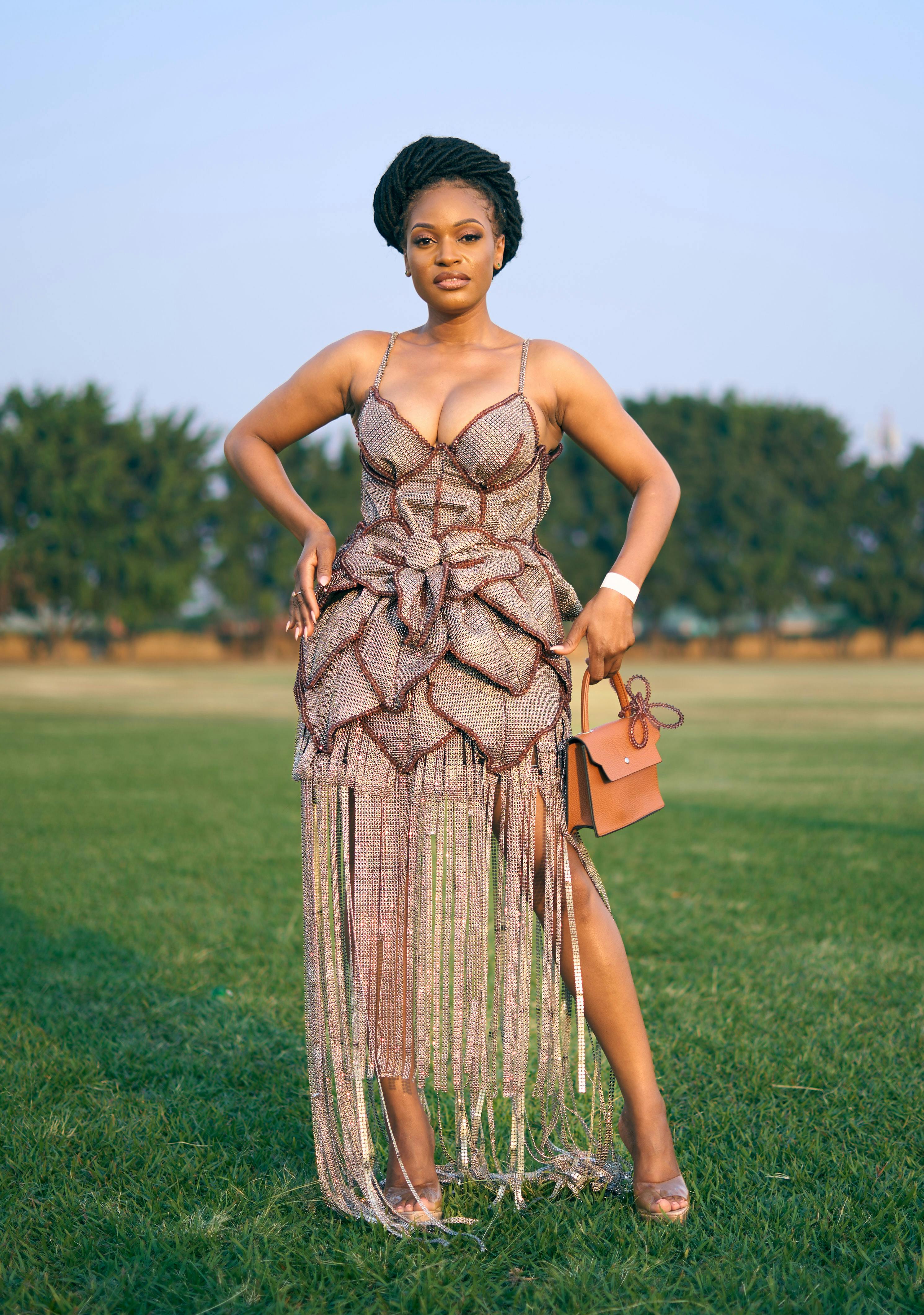 Stylish woman in a chic dress poses confidently in a natural outdoor setting.